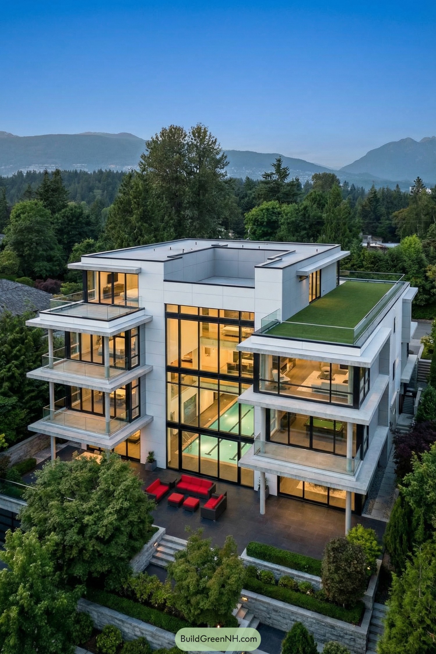 Modern multi level glass house with rooftop lawn surrounded by lush trees and distant mountains