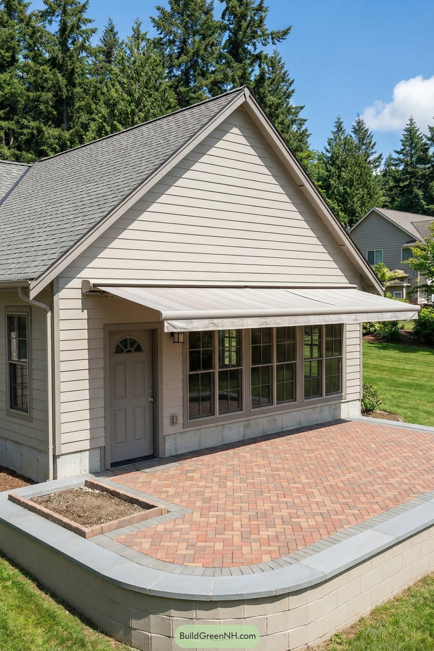 Raised brick courtyard patio outside beige house with large windows and retractable awning