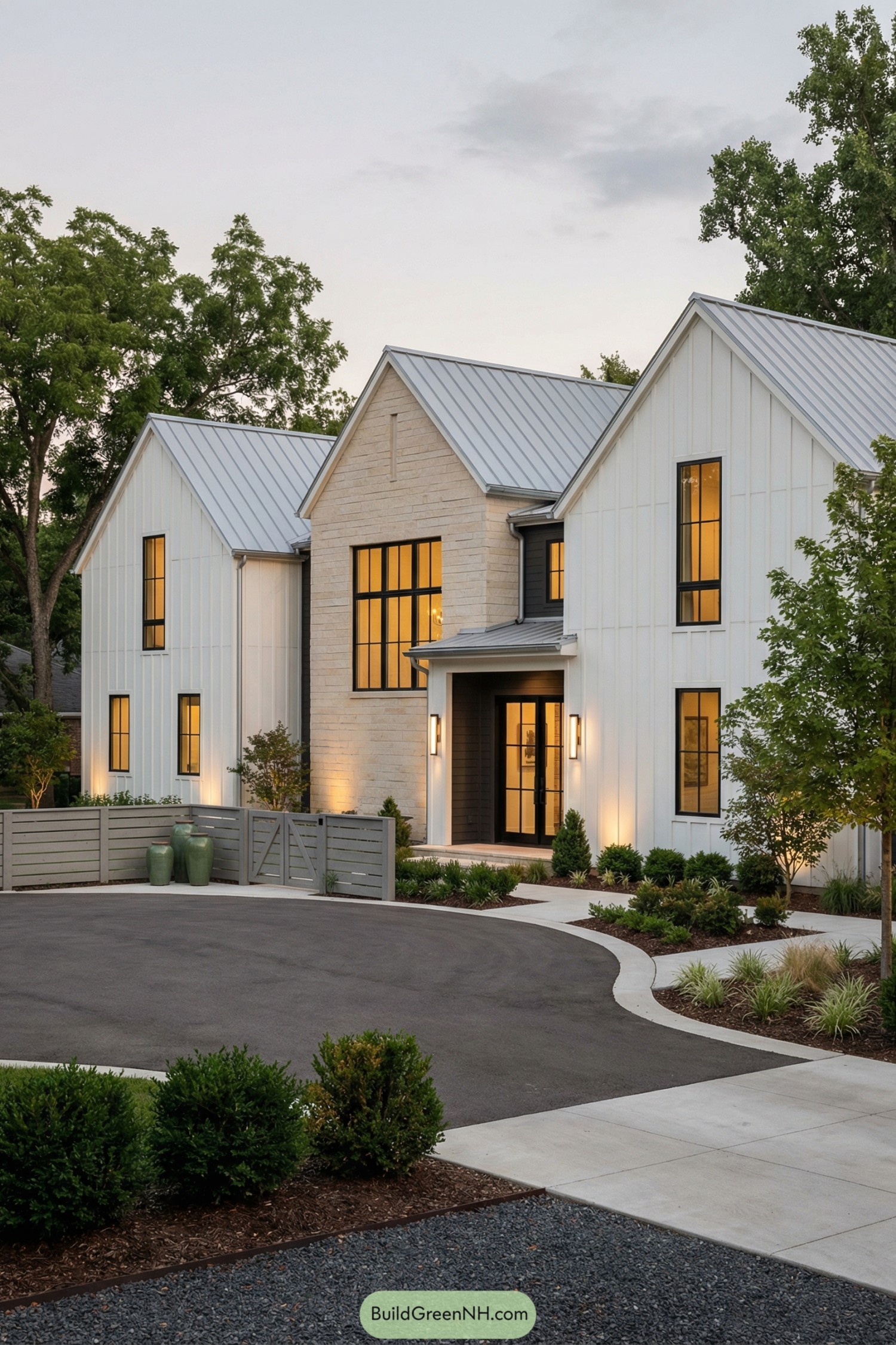 Modern white farmhouse with metal roofs and warm interior lighting at dusk