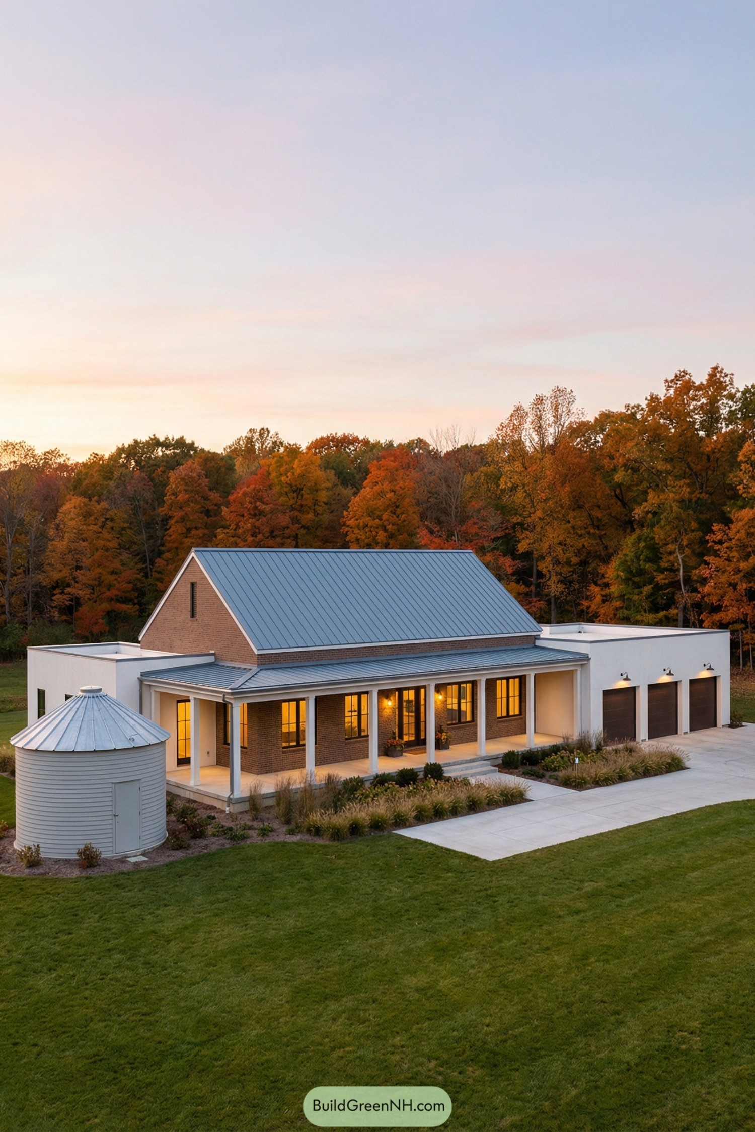 Single-story modern farmhouse with metal roof, long front porch, and small silo-shaped outbuilding in a green field