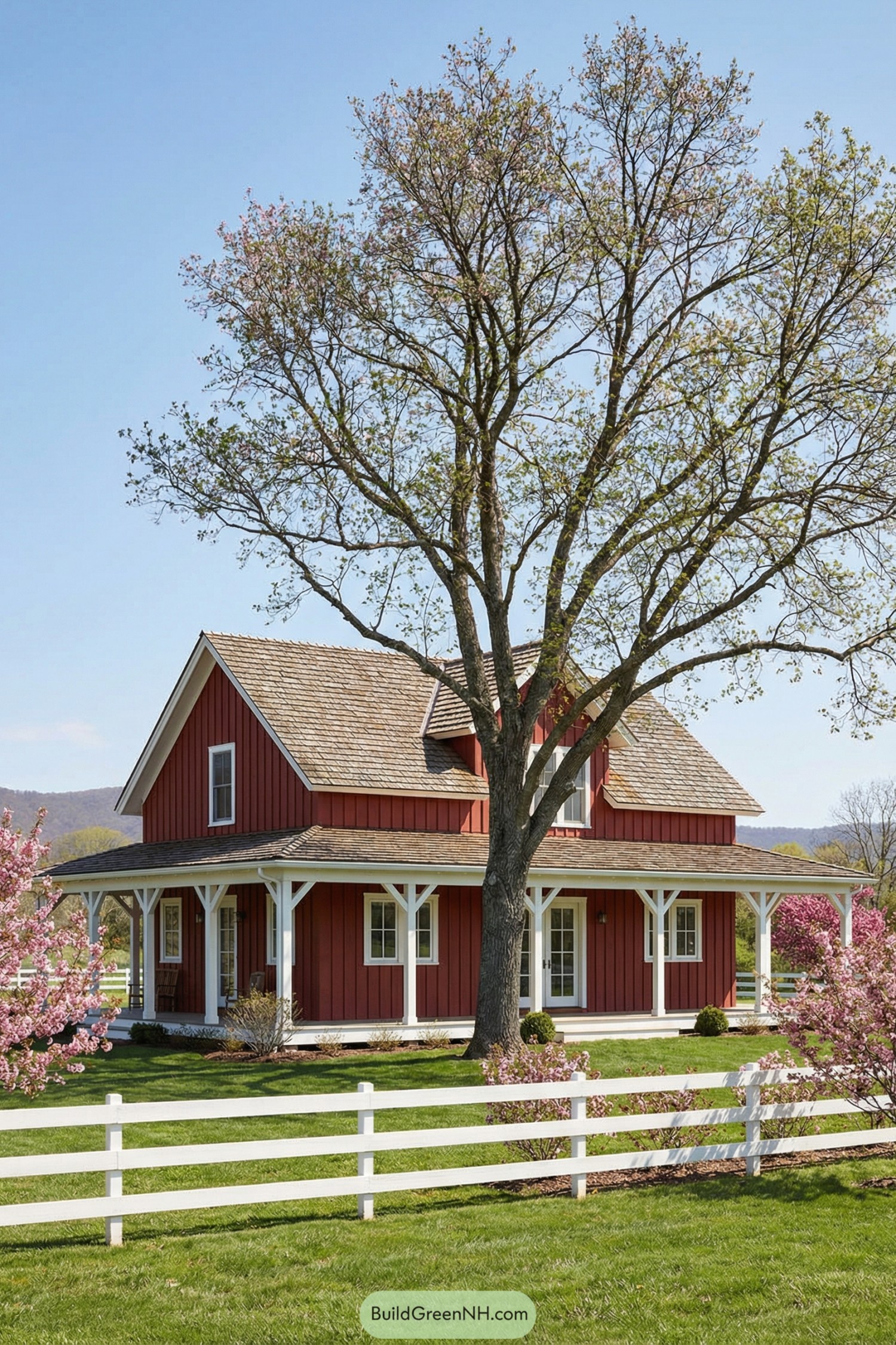 Red farmhouse-style ranch with wraparound porch, large shade tree, and white rail fence in a green countryside setting