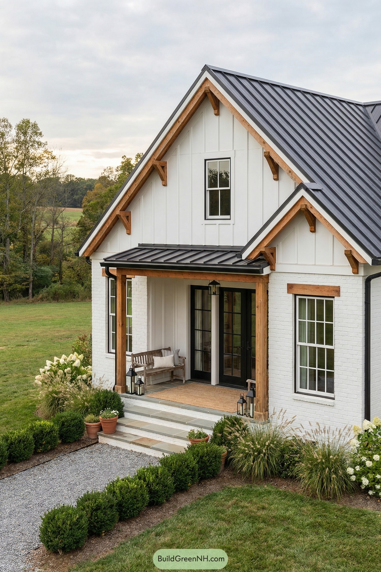 White farmhouse with dark metal roof and wood-trimmed front porch surrounded by neat landscaping