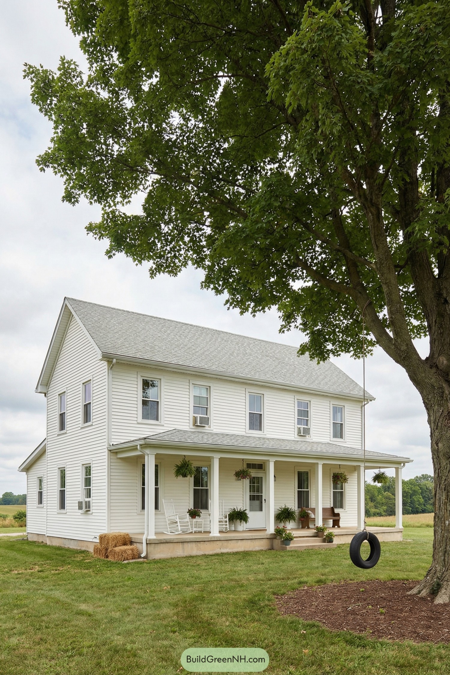 Two-story white farmhouse with long front porch, rocking chairs, hanging plants, and nearby tire swing under a large tree. Surrounded by open grassy yard and distant fields