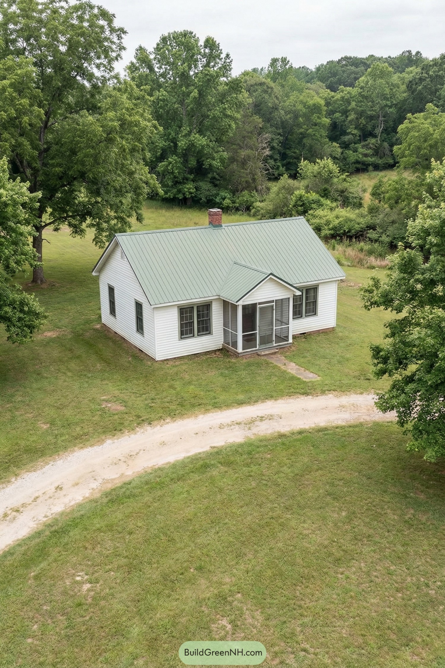 Small white cottage with green metal roof and screened front porch set in a grassy clearing