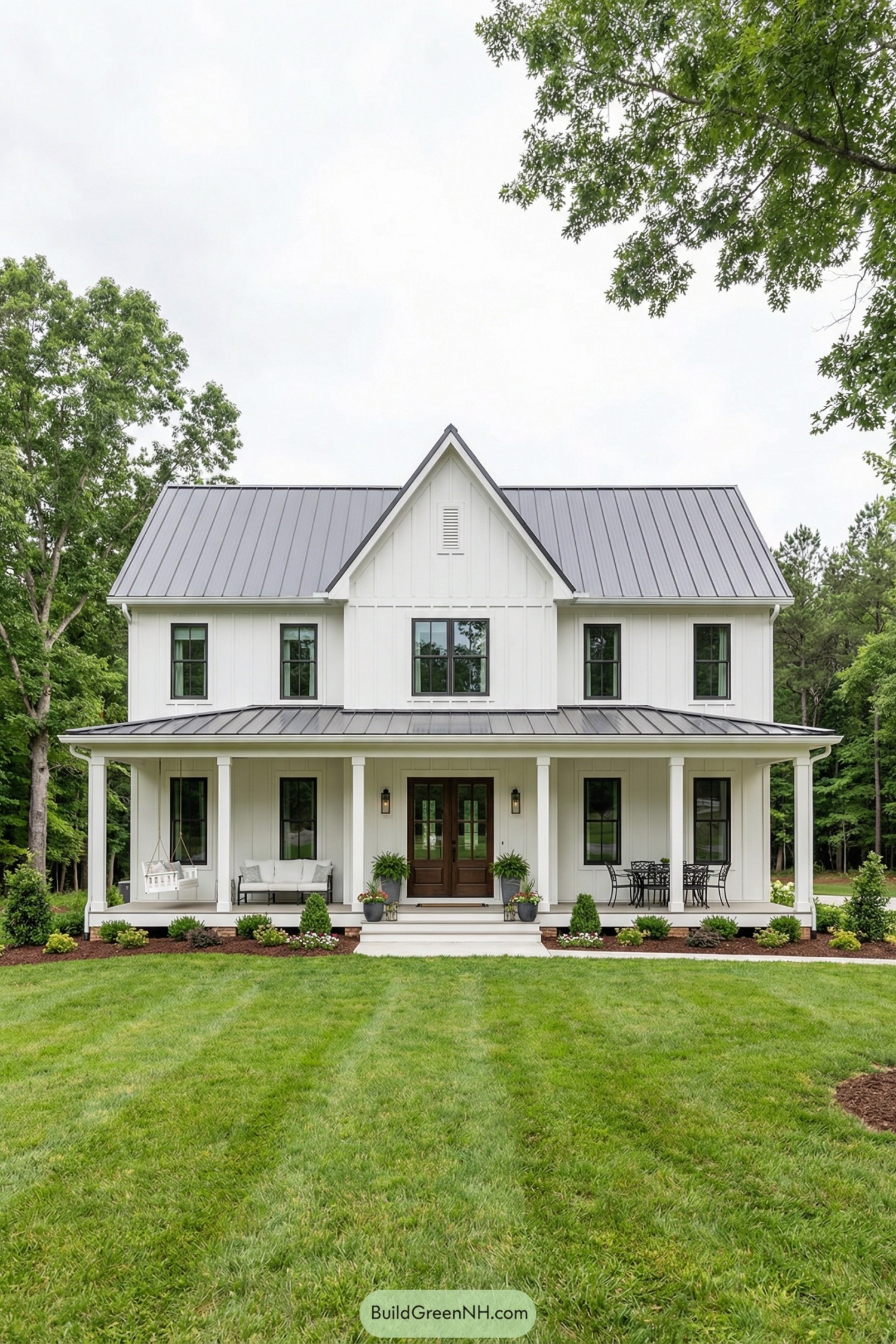 White farmhouse with metal roof and full front porch surrounded by lawn and trees