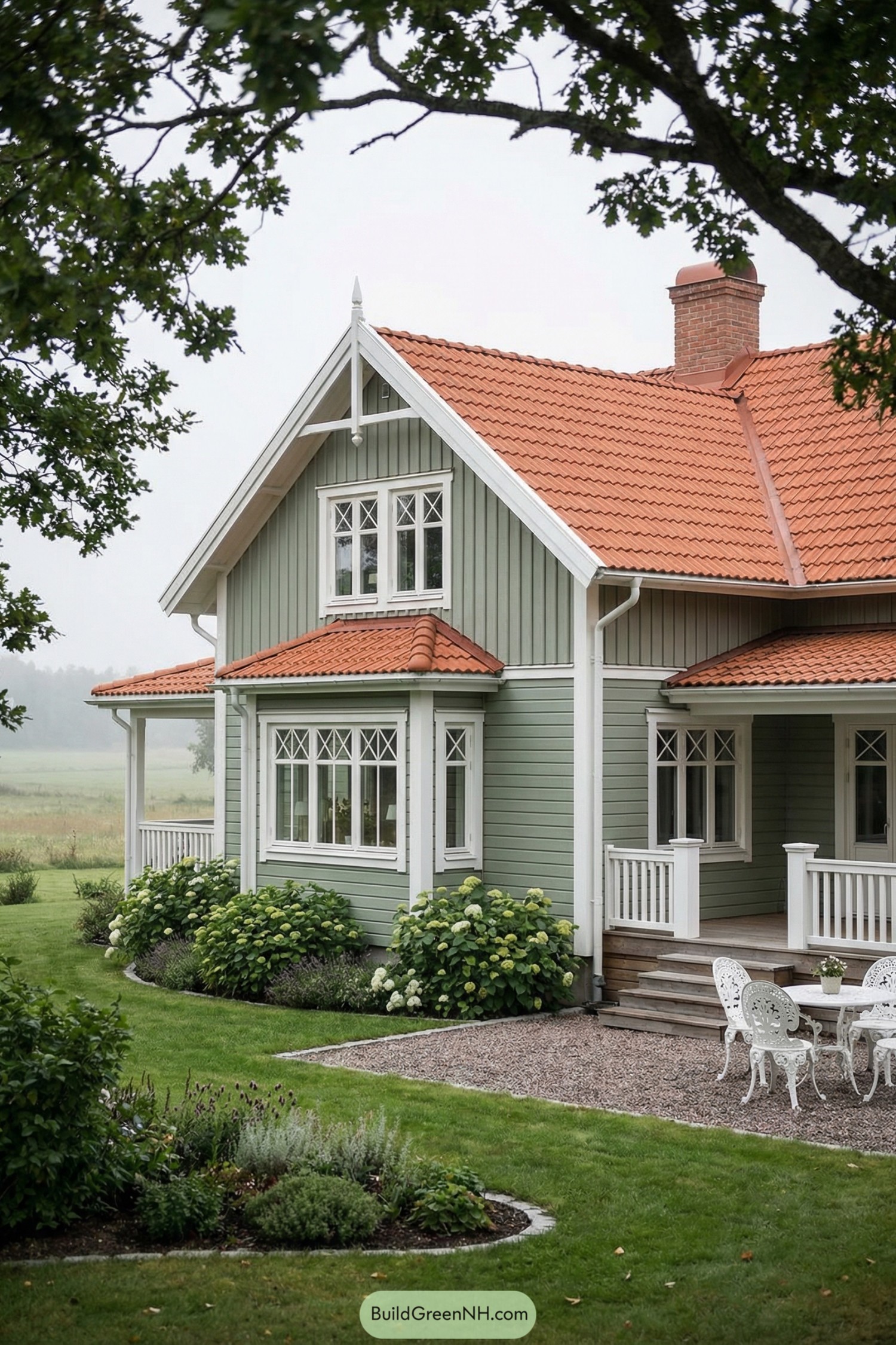 Sage green country house with red tile roof and white trim beside a small garden patio