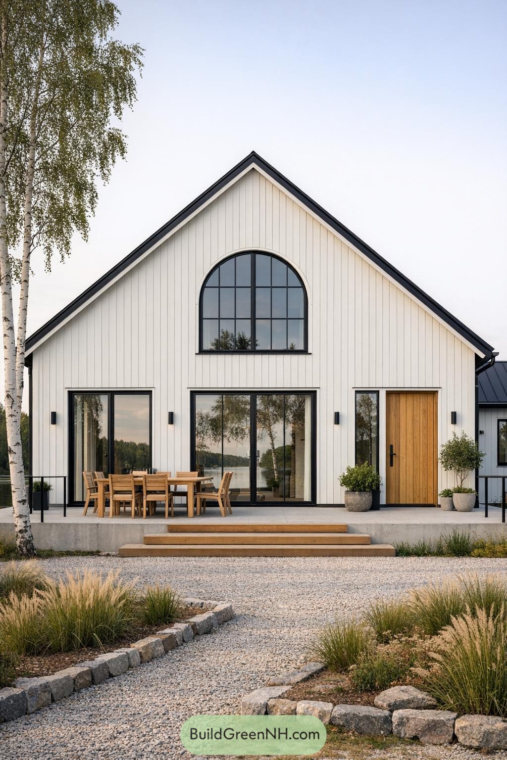 Modern white Scandinavian villa with tall black-framed windows and wood accents facing a lakeside patio