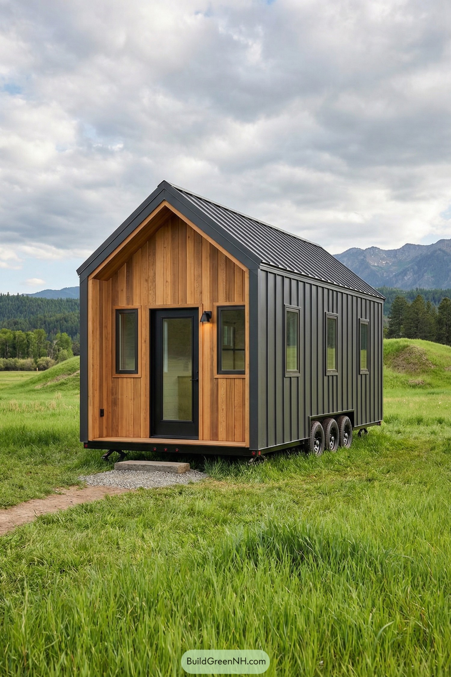 Compact black metal and wood tiny house on triple-axle trailer in a green field