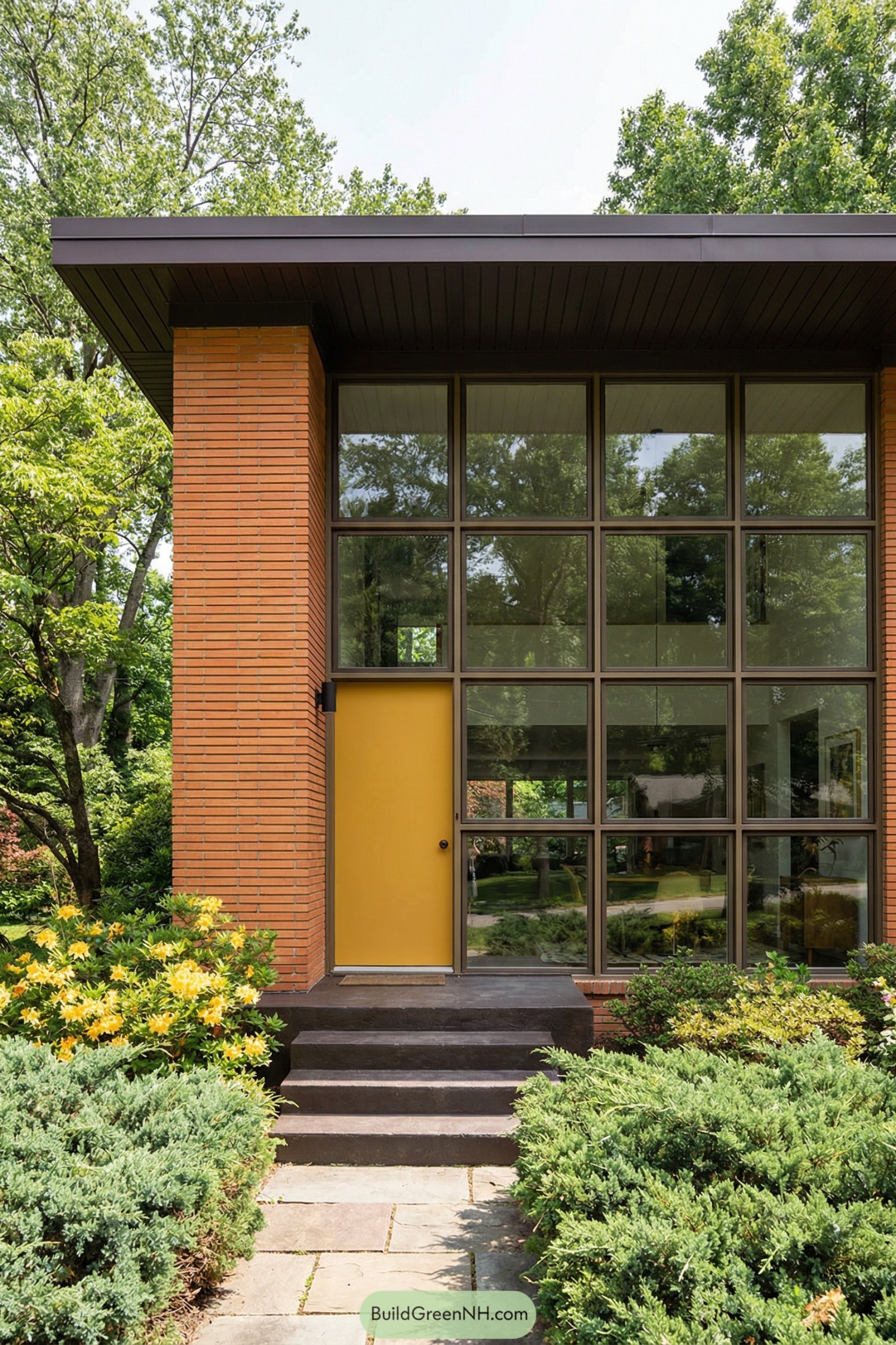 Tall midcentury brick entry with yellow door and large grid of windows