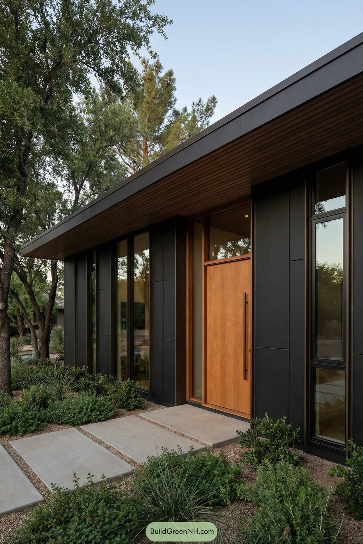 Modern black midcentury house with tall windows and warm wood front door surrounded by lush landscaping
