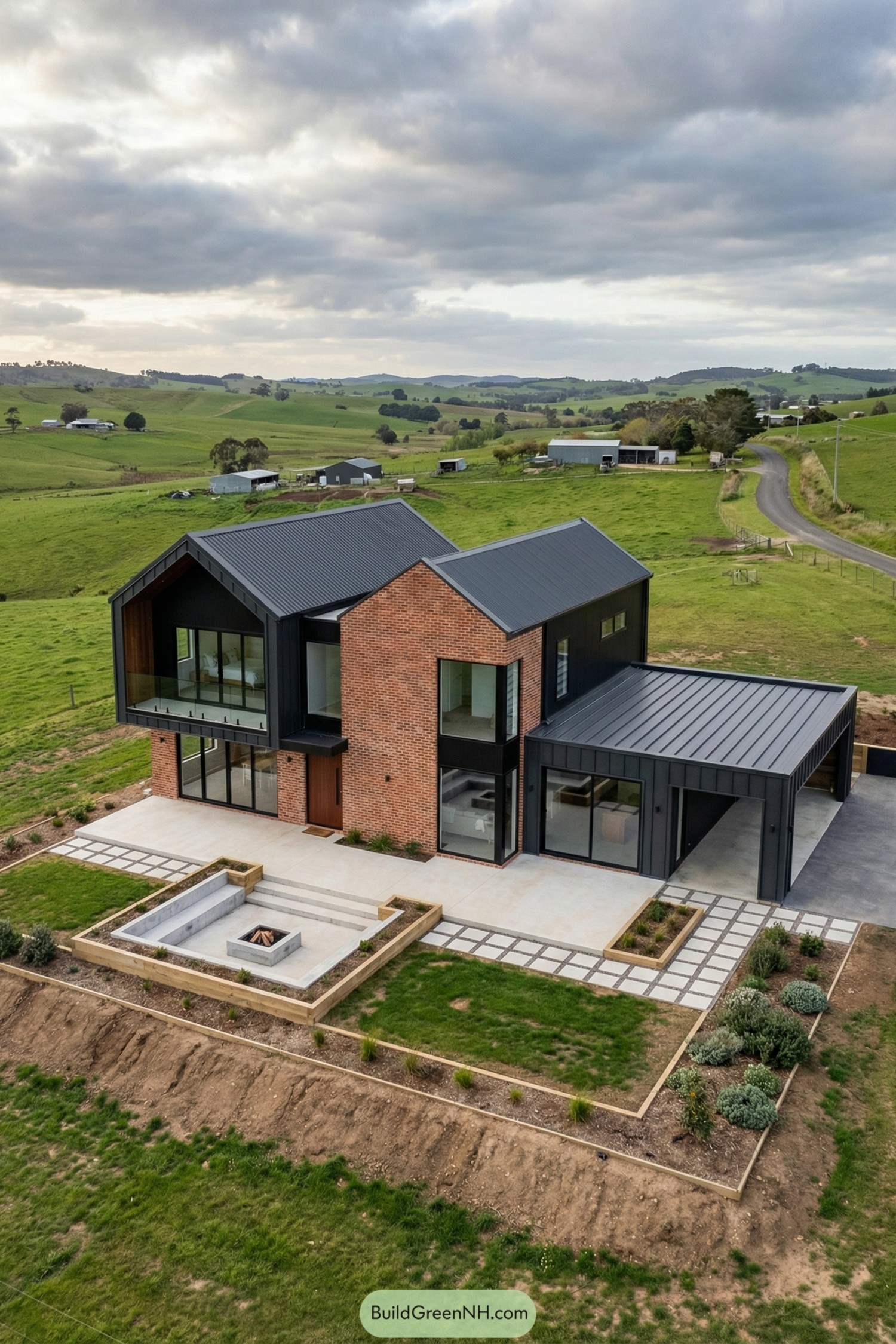 Modern brick and black metal farmhouse with large windows overlooking rolling green countryside and a sunken outdoor fire pit terrace