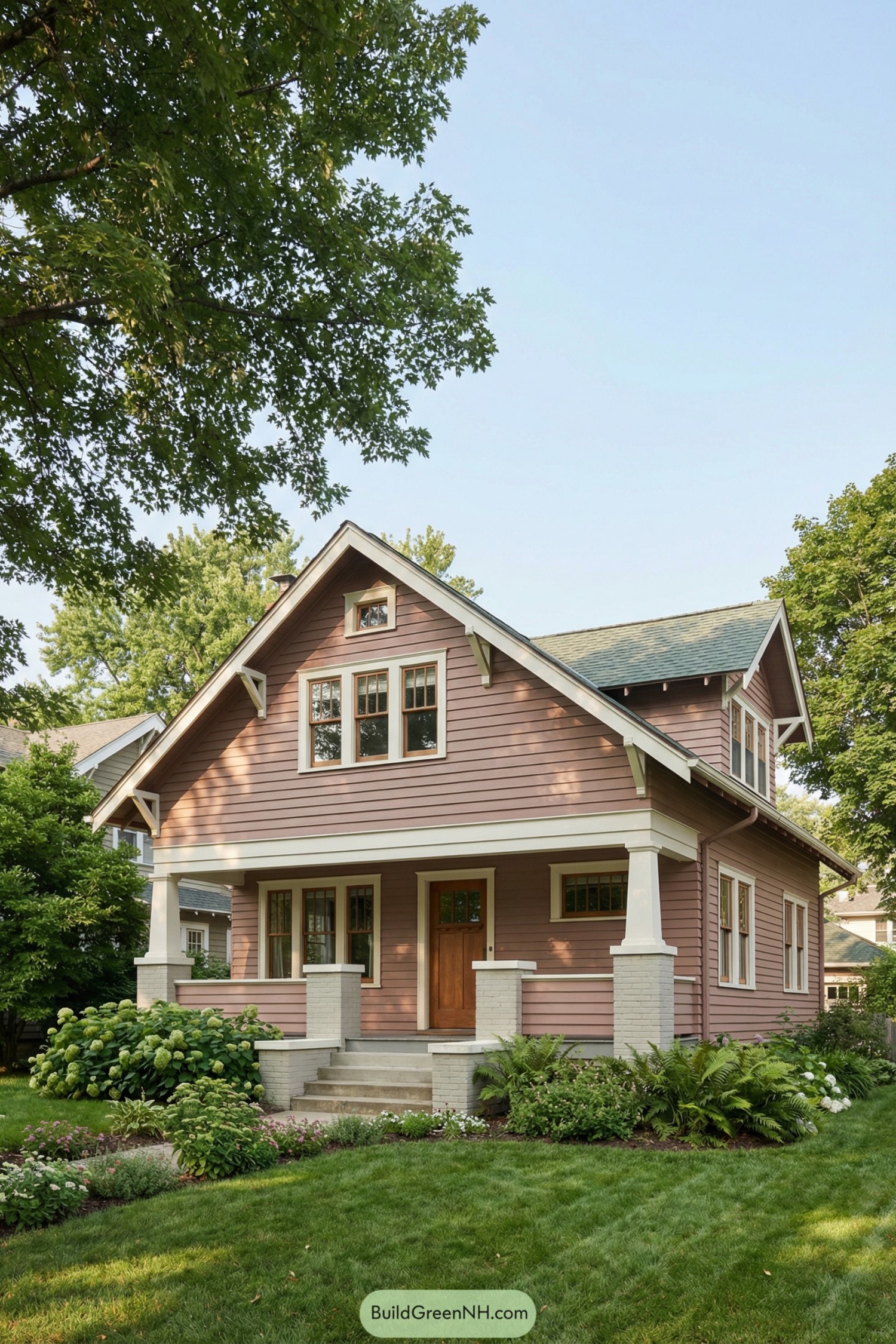 Warm rose-clad craftsman bungalow with deep front porch, tapered porch columns, and lush green garden
