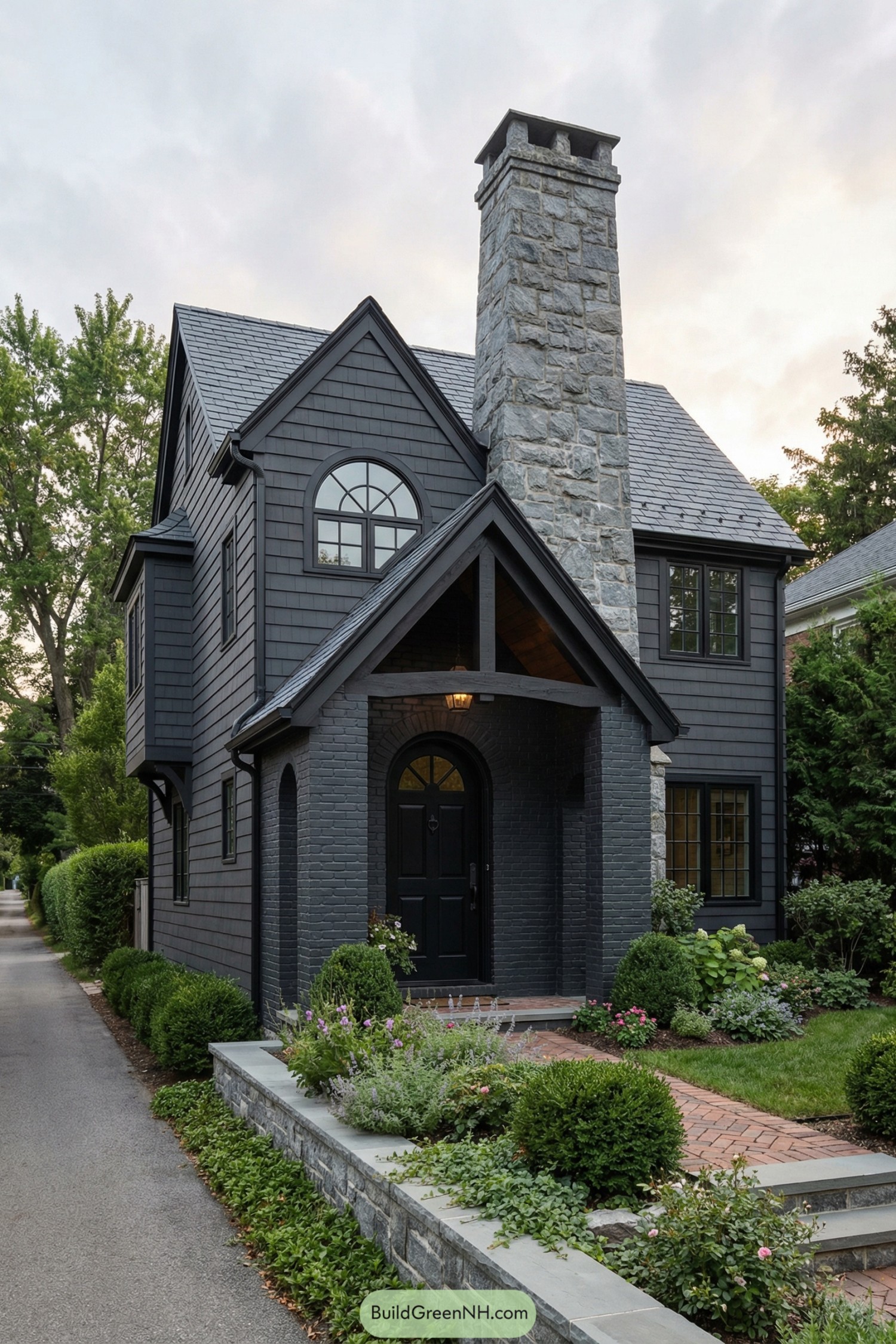Dark shingle cottage with tall stone chimney and lush front garden