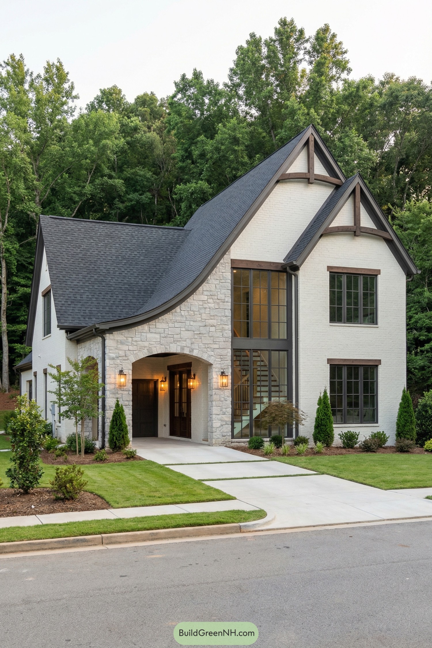 Light stone and white brick cottage with tall windows, steep dark roof, and arched entry framed by simple landscaping