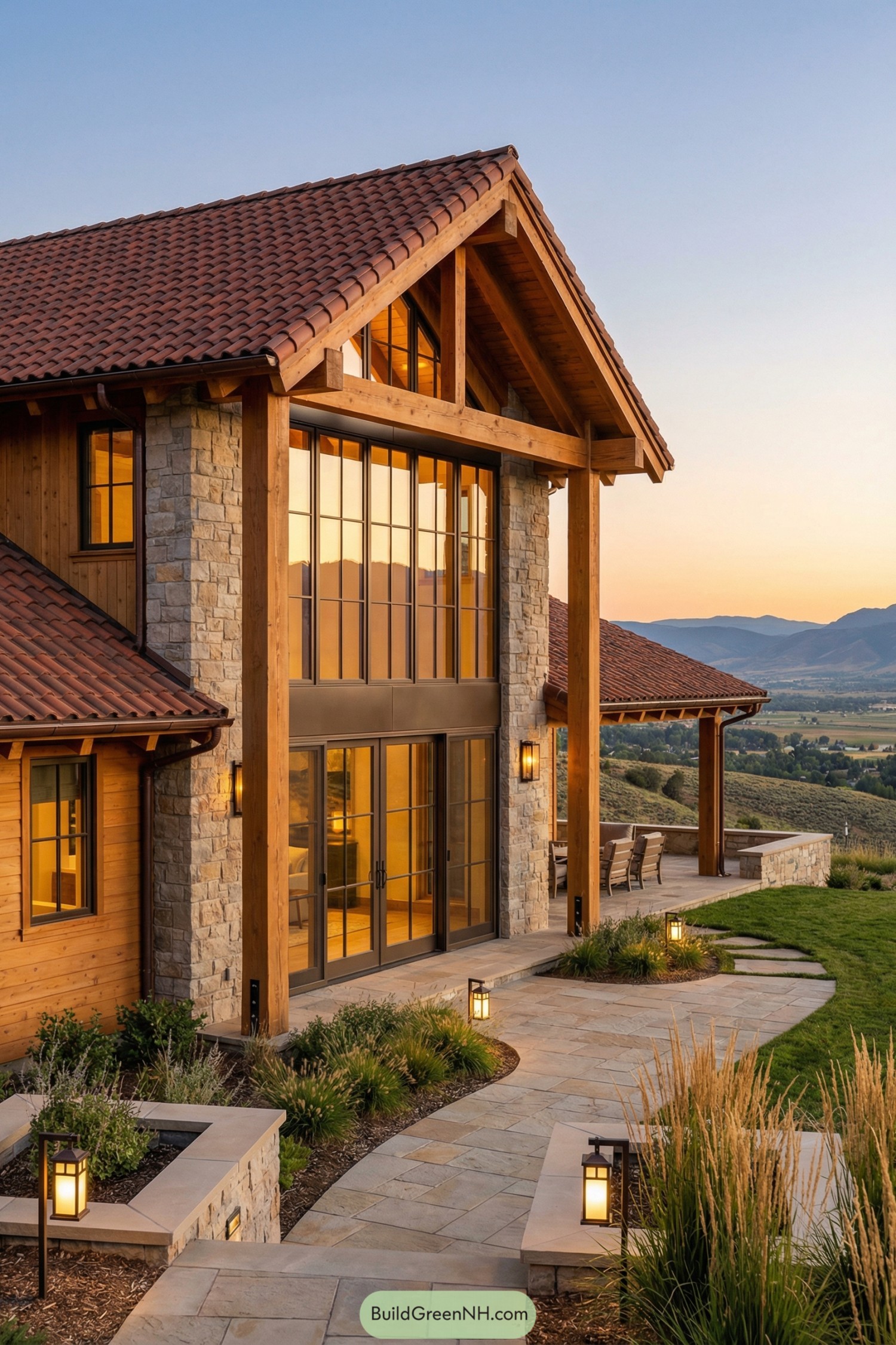 Warm stone and timber cottage with tall glass front overlooking rolling hills at sunset