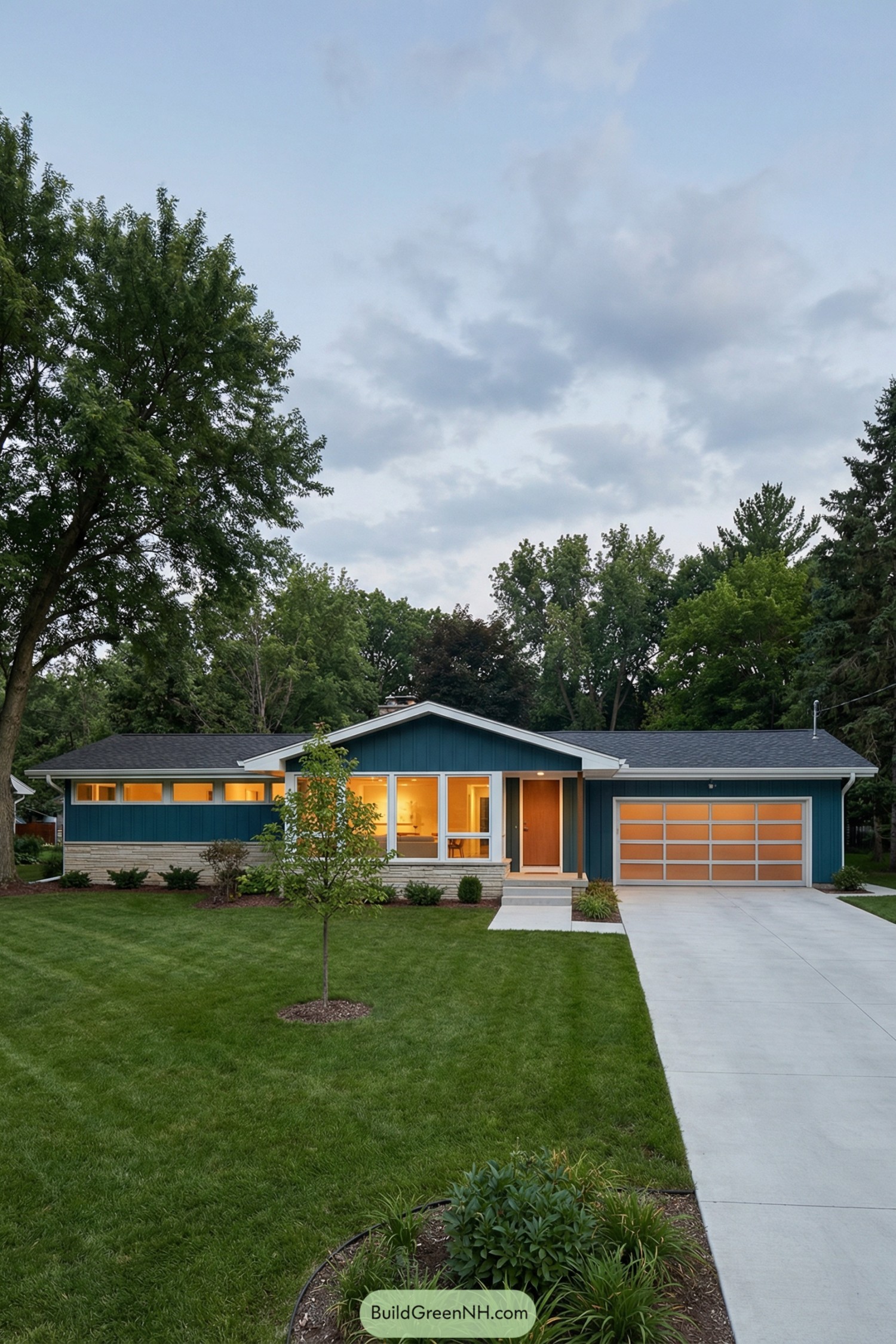 Blue single story home with wide front windows and lit interiors at dusk