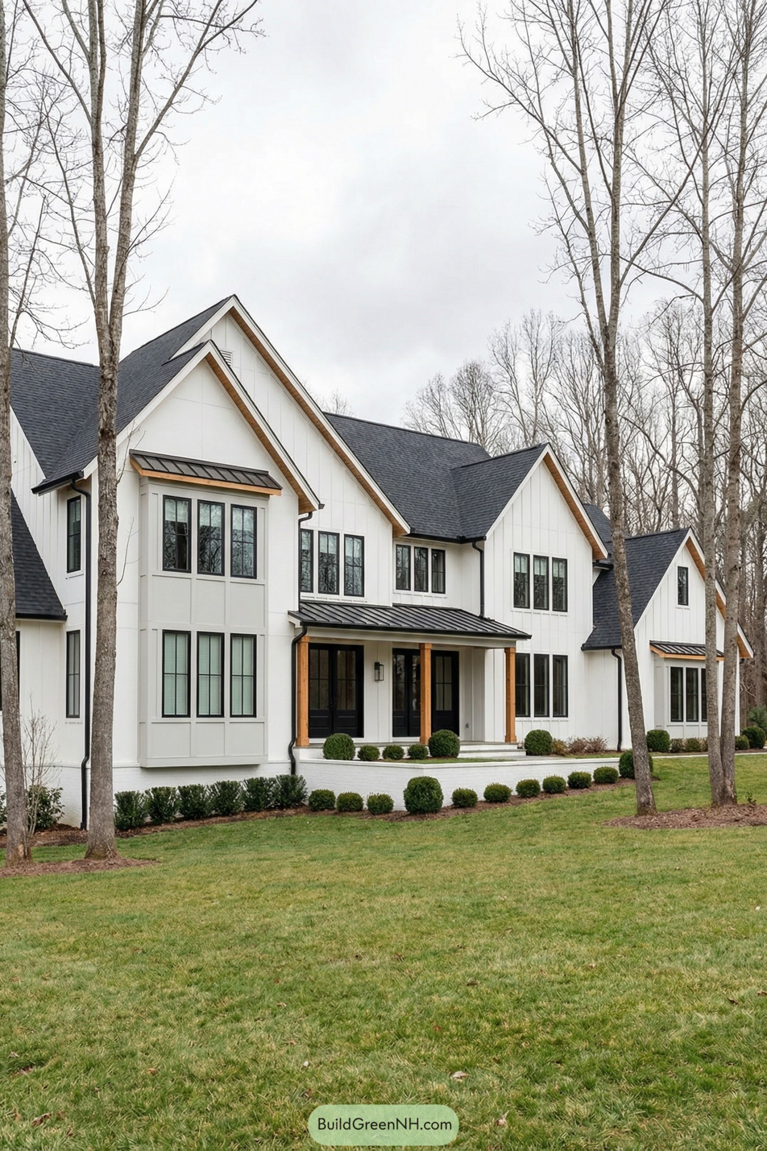 Spacious modern white farmhouse with black roof and wood accents set among tall trees
