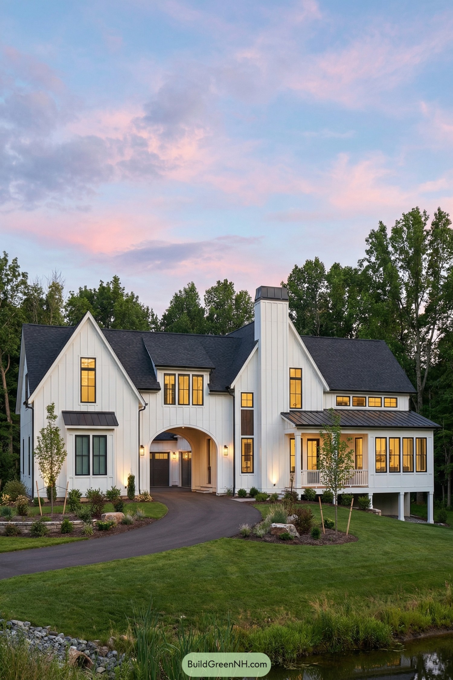 White modern farmhouse with black roof, archway drive, and glowing windows at sunset