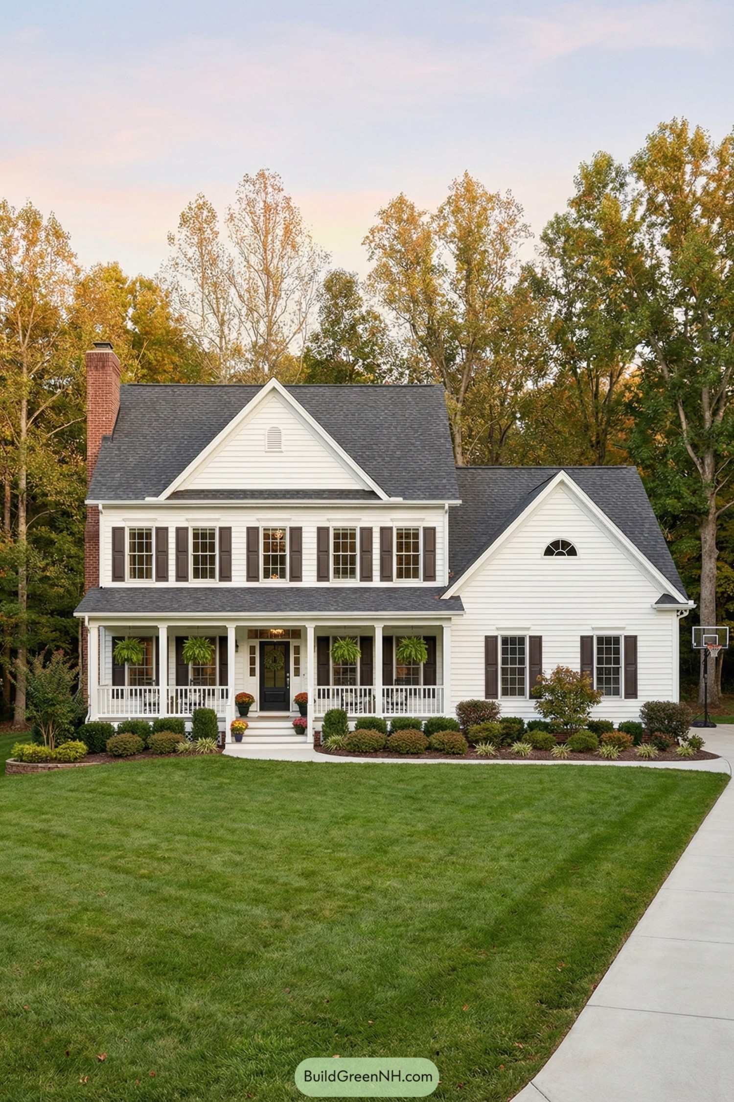 Two story white farmhouse with wide front porch dark roof and neatly landscaped front yard