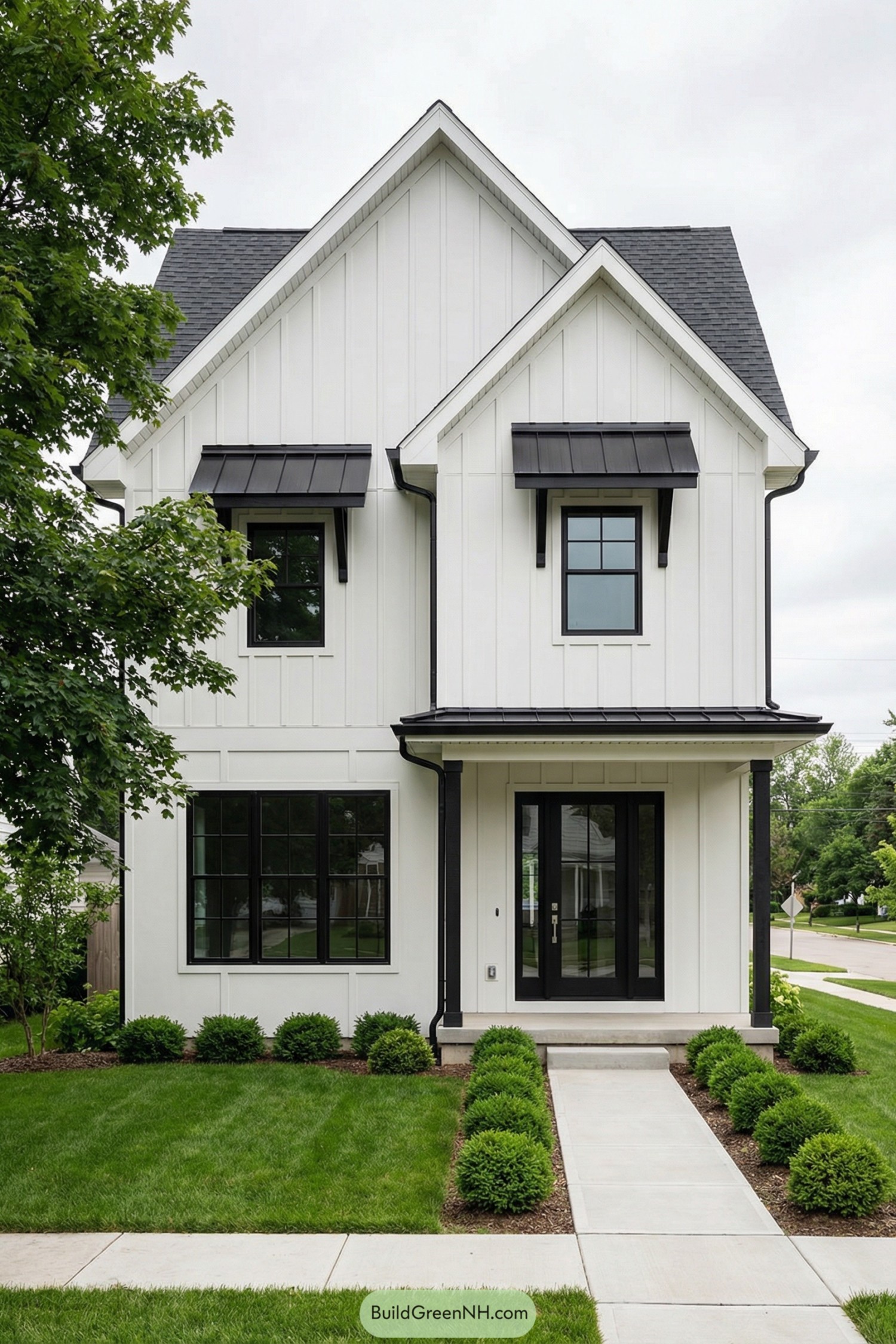 White two story gabled house with black metal awnings black framed windows and manicured front walk and lawn