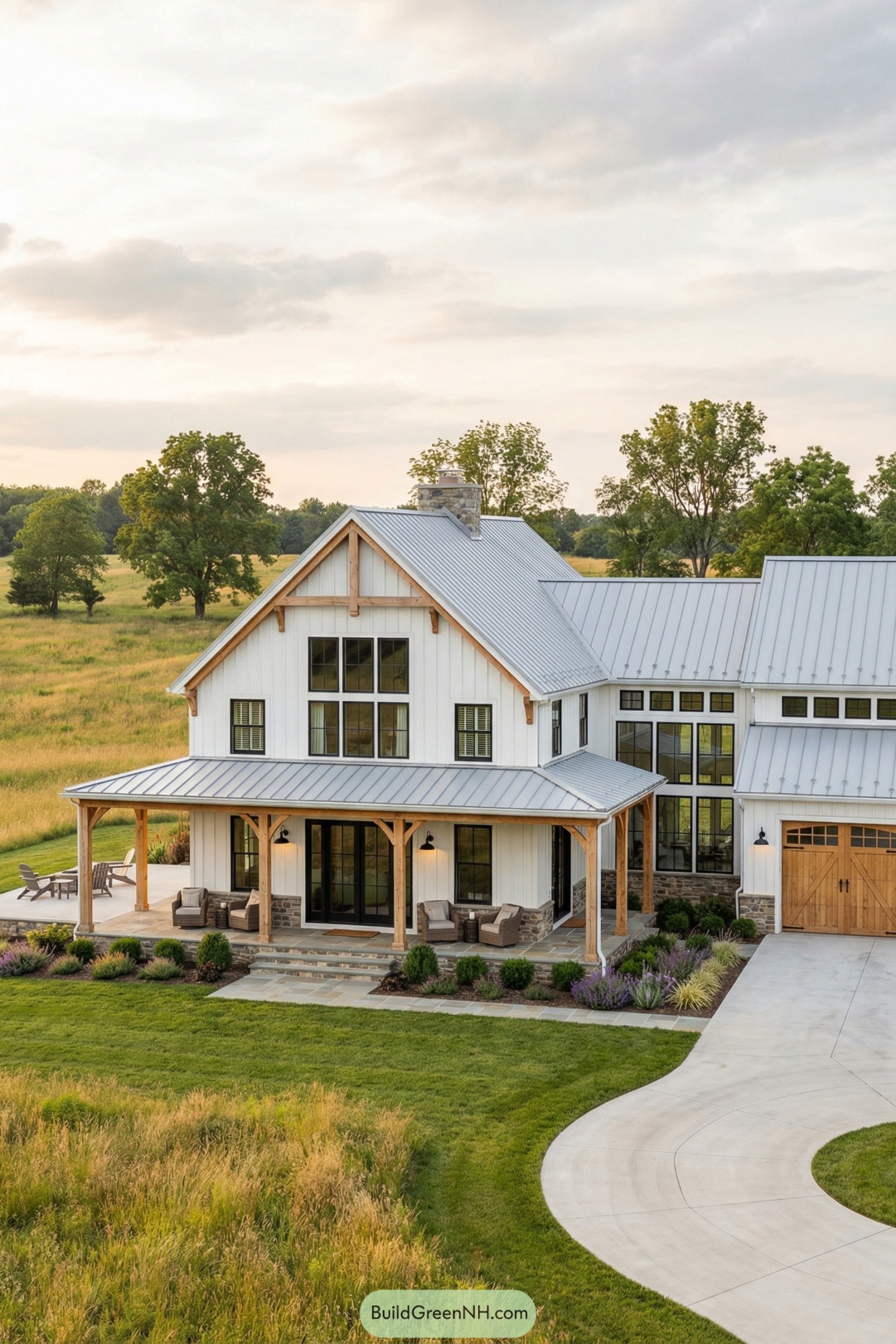 White board and batten colonial barndominium with metal roof, wraparound porch, and stone accents set in open countryside