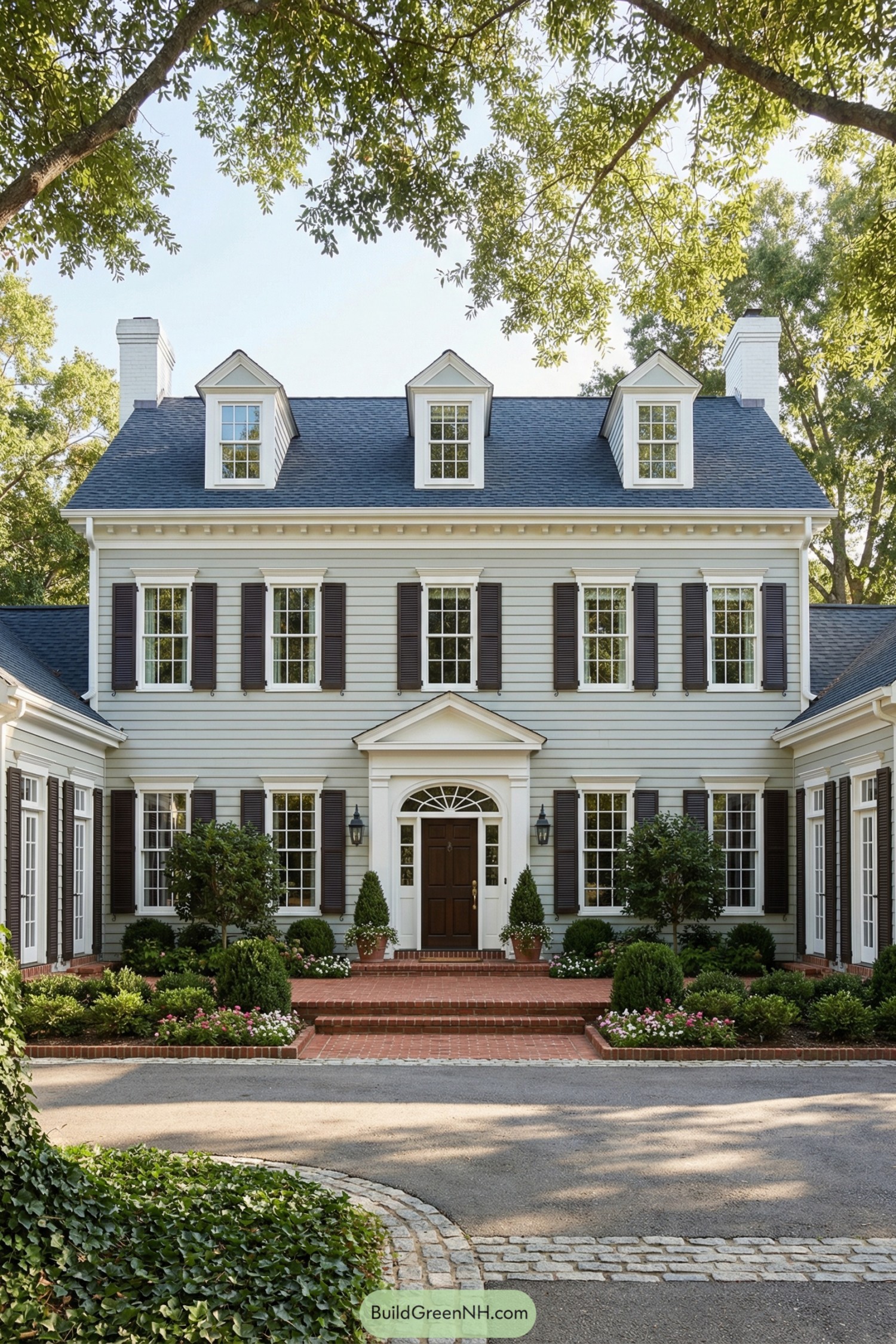 Traditional colonial home with gray siding, dark shutters, and brick entrance framed by manicured landscaping