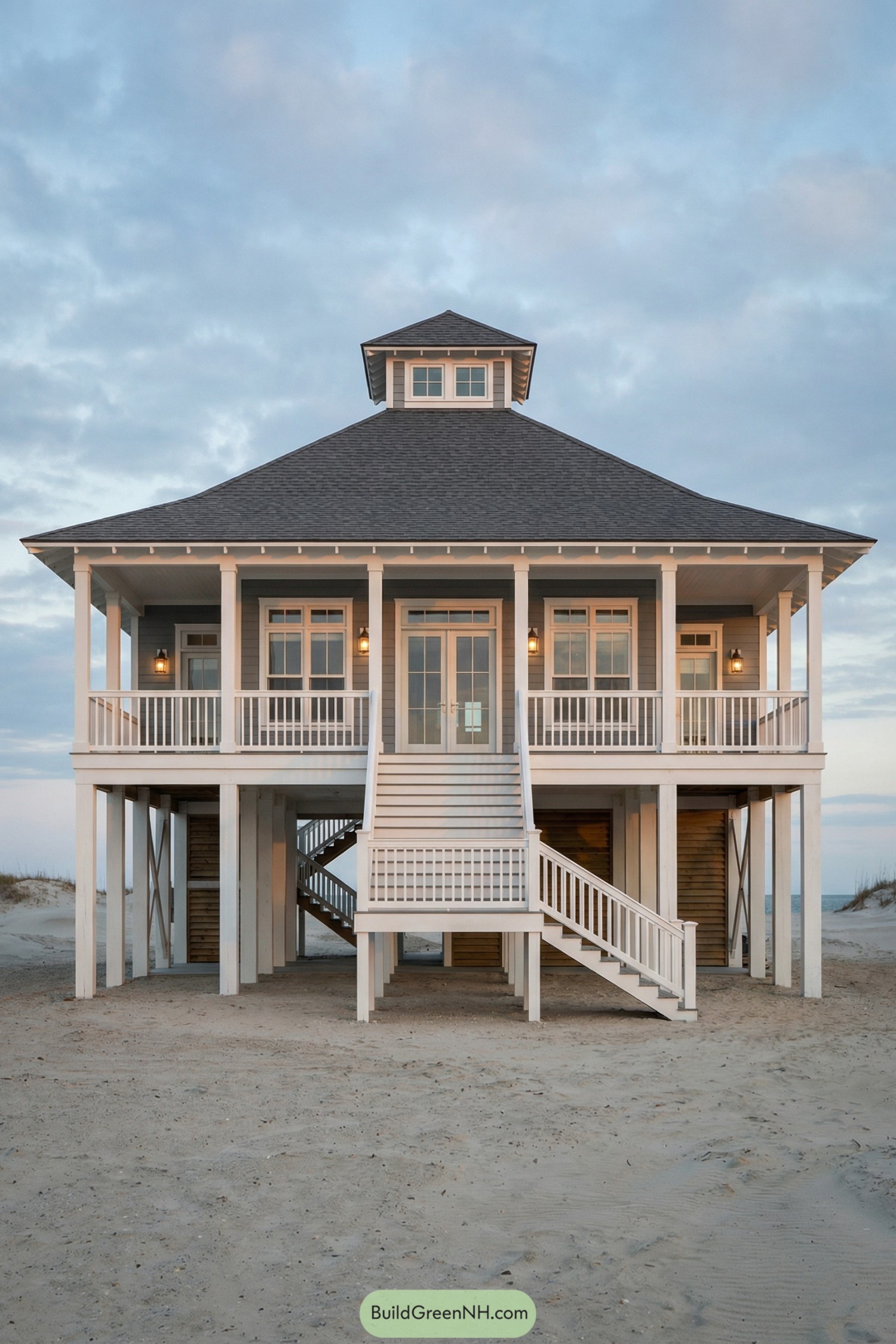 Elevated gray beach house with wraparound porch, central staircase, and cupola roof