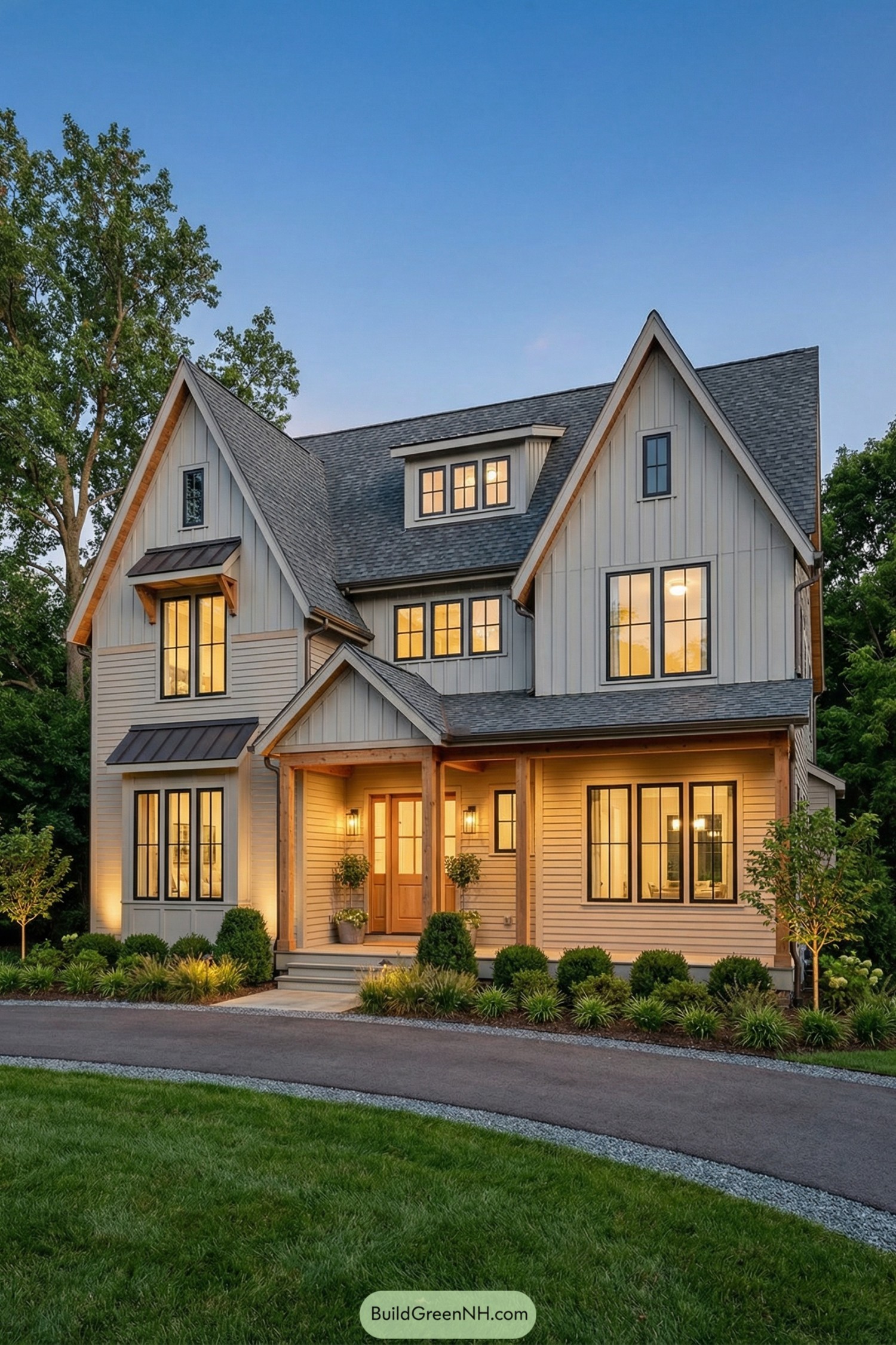 high-res photo of cute country house, modern farmhouse facade with asymmetrical massing and multiple front gables, light warm-beige horizontal siding on lower level and light gray vertical board-and-batten on gable ends, natural wood trim and posts adding warm contrast, rectangular two-story shape with single-story side wings and a shallow front porch zone, materials include painted wood or fiber-cement cladding, natural wood columns and soffits, dark metal accents over bay windows, roofing in dark gray architectural shingles with varied rooflines, front-facing steep gables and a central shed dormer, wide black-framed grid windows in varied sizes including tall double casements, grouped picture windows, and smaller dormer windows, front door centered under a gabled porch with natural wood door and sidelights, covered porch running across much of the facade with slender square wood columns and simple rail-free edge, paved driveway curving along the front with a narrow gravel edge, neat foundation plantings with boxwood shrubs, ornamental grasses, low hedges, and young trees in planters aligned along the porch, manicured green lawn in foreground with crisp edges, mature trees and dense greenery framing the property in the background under a clear dusk sky, warm exterior lighting washing the facade and highlighting textures, single real-life photo, high-resolution, architectural photography, soft lighting, cinematic composition, strictly no collages
