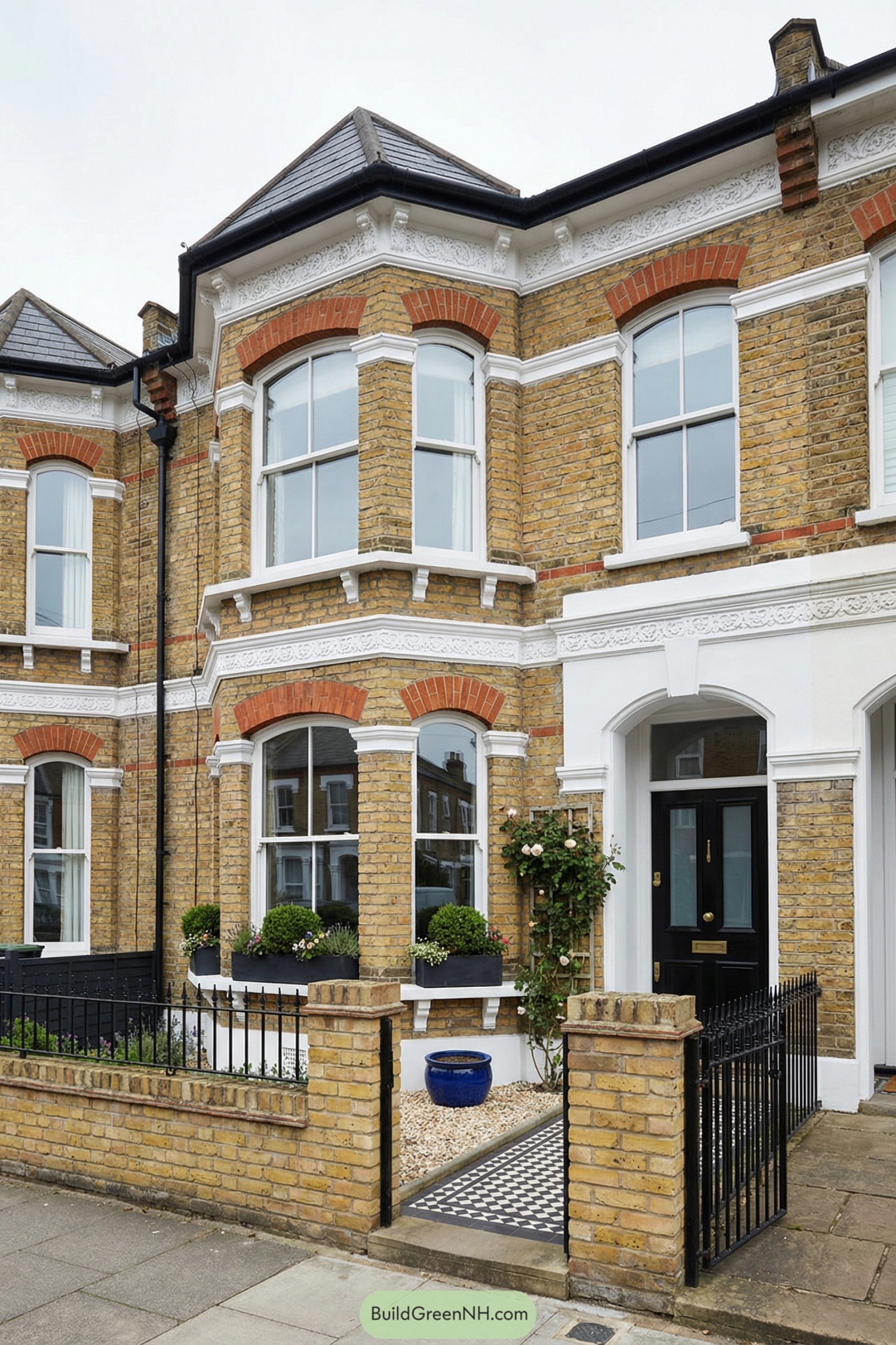 Victorian yellow-brick townhouse with bay windows, ornate white trim, and a small gated front garden