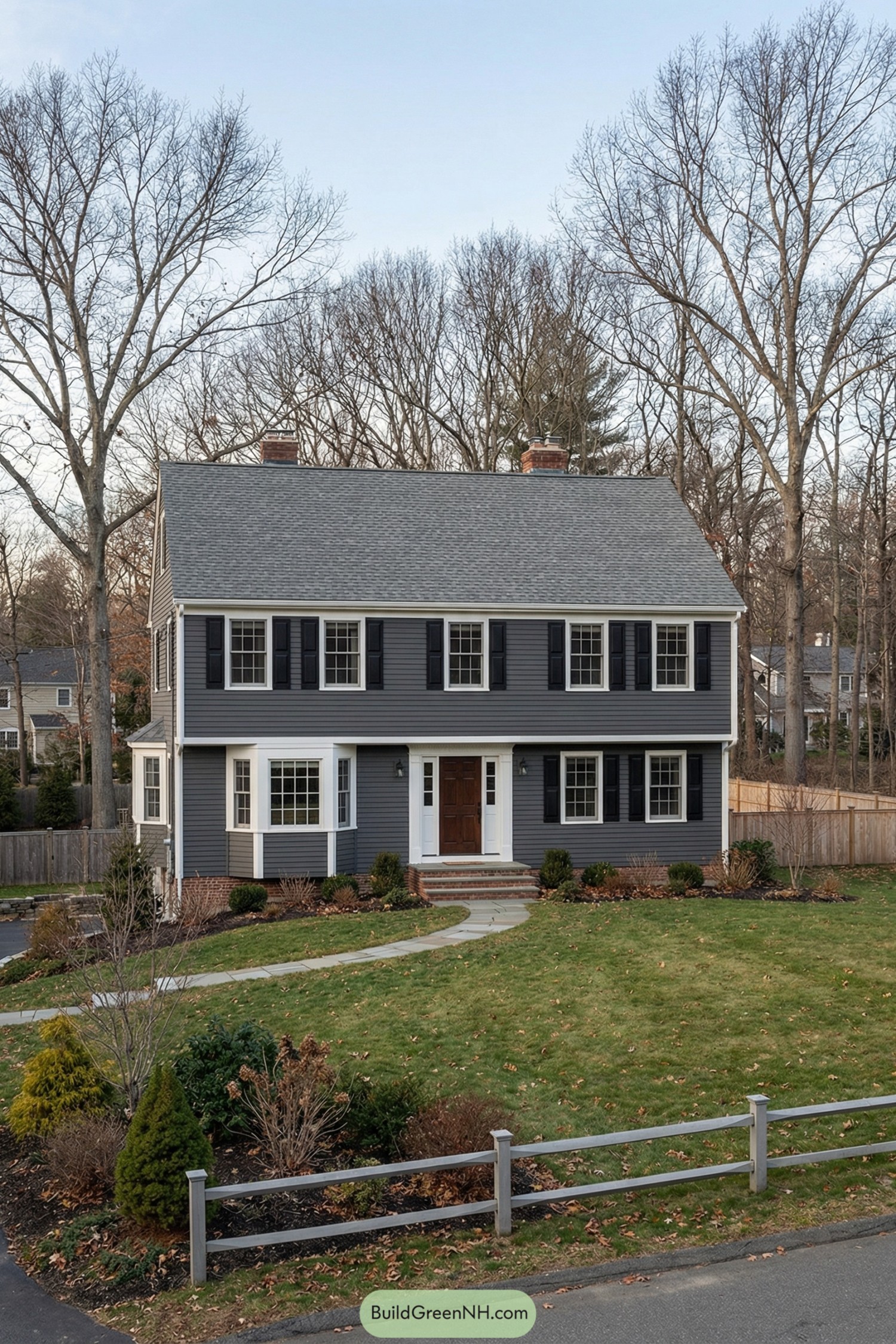 Two story gray garrison colonial house with black shutters, white trim, and a central front door set on a lawn with curved walkway