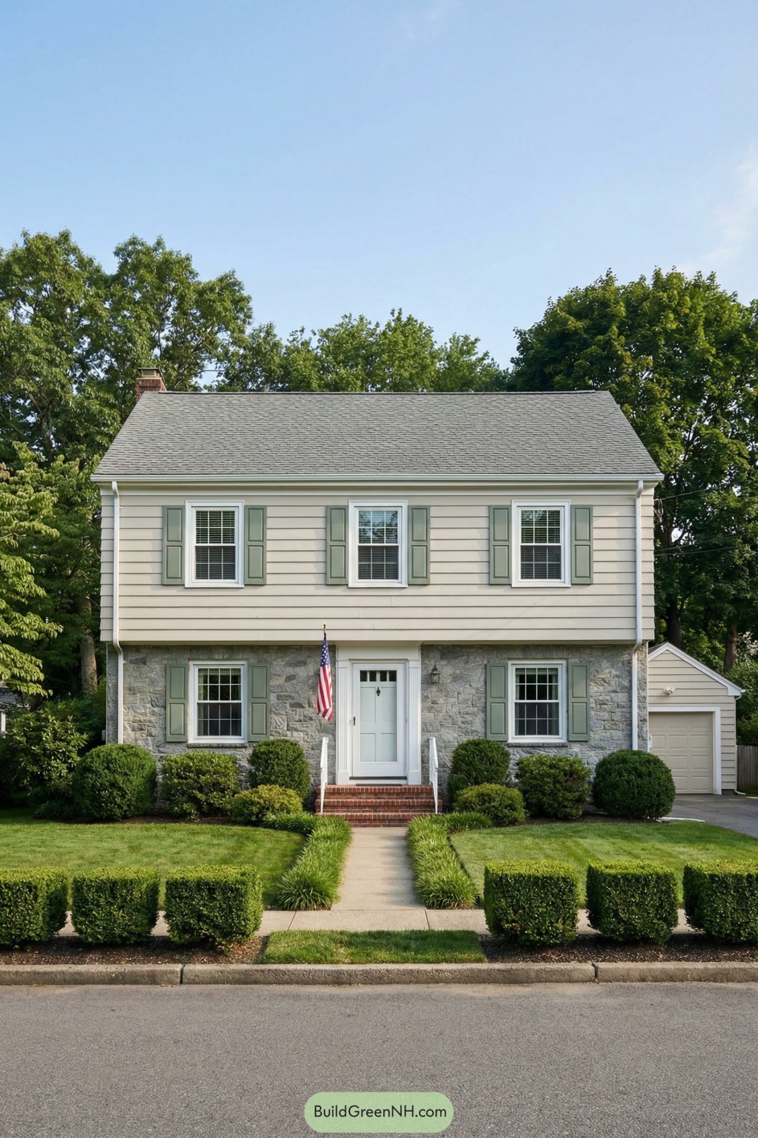 Two story garrison colonial with stone base and pale siding, centered entry, and manicured front yard