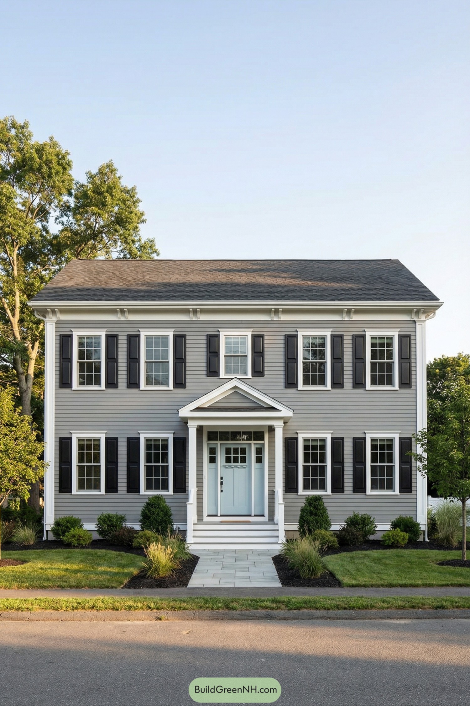 Two story gray garrison style house with black shutters a central portico and simple front landscaping