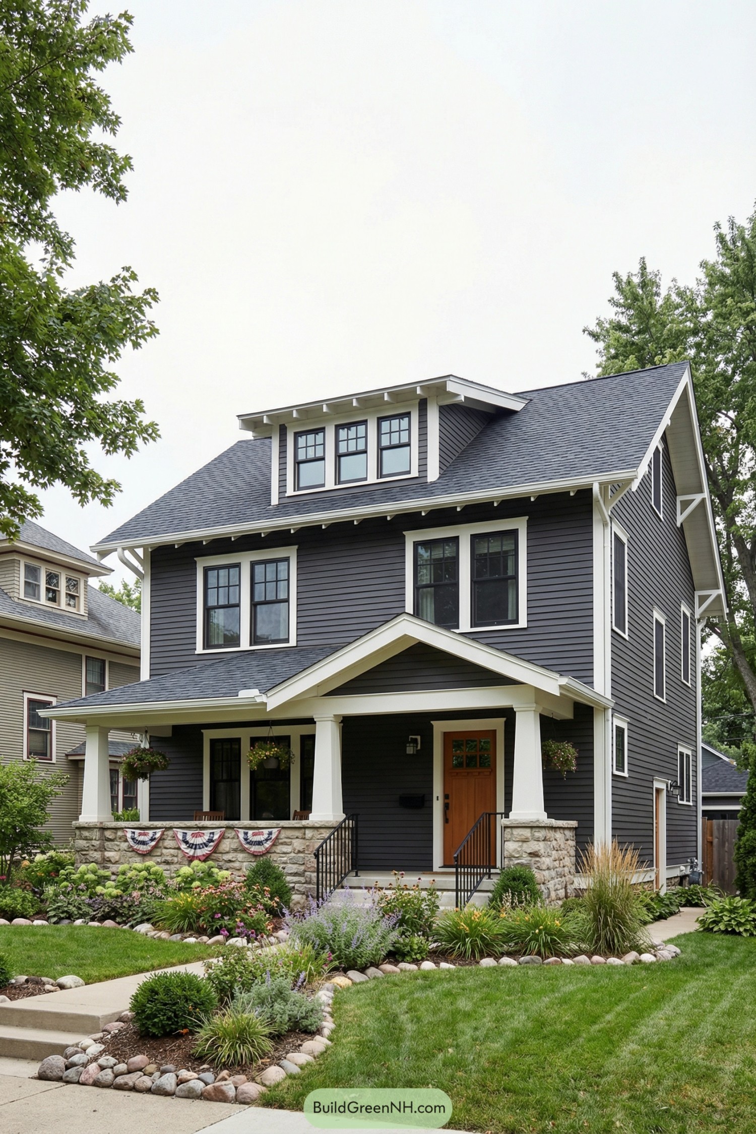 Dark gray three story craftsman house with white trim and stone front porch pillars