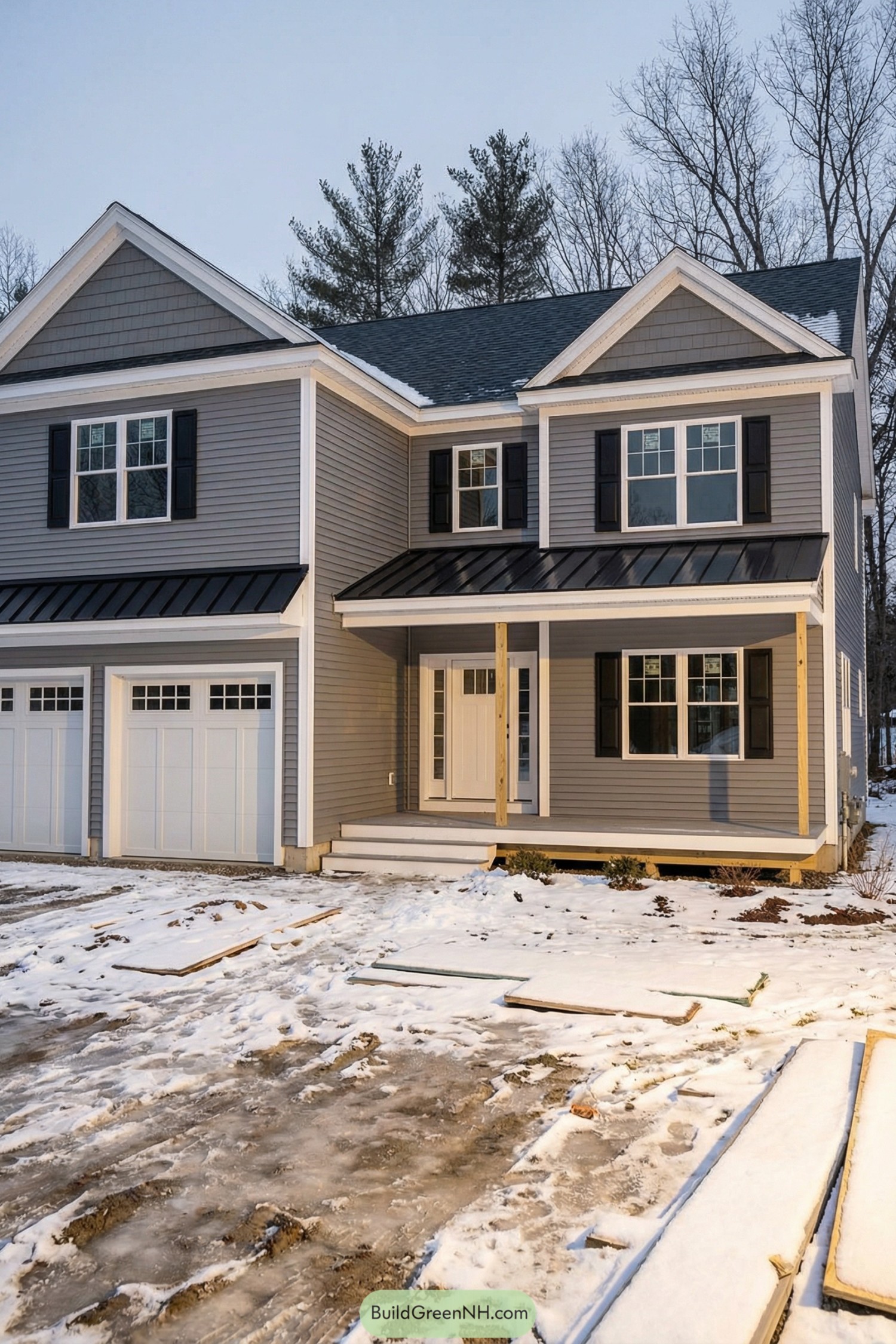 Two story gray house with white trim black shutters and double garage in a snowy yard