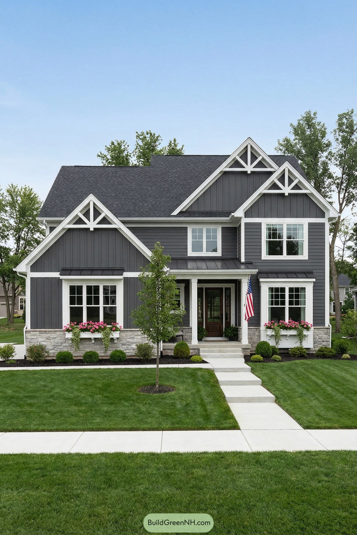 Gray two story house with white trim and stone base framed by tidy lawn and blooming window boxes