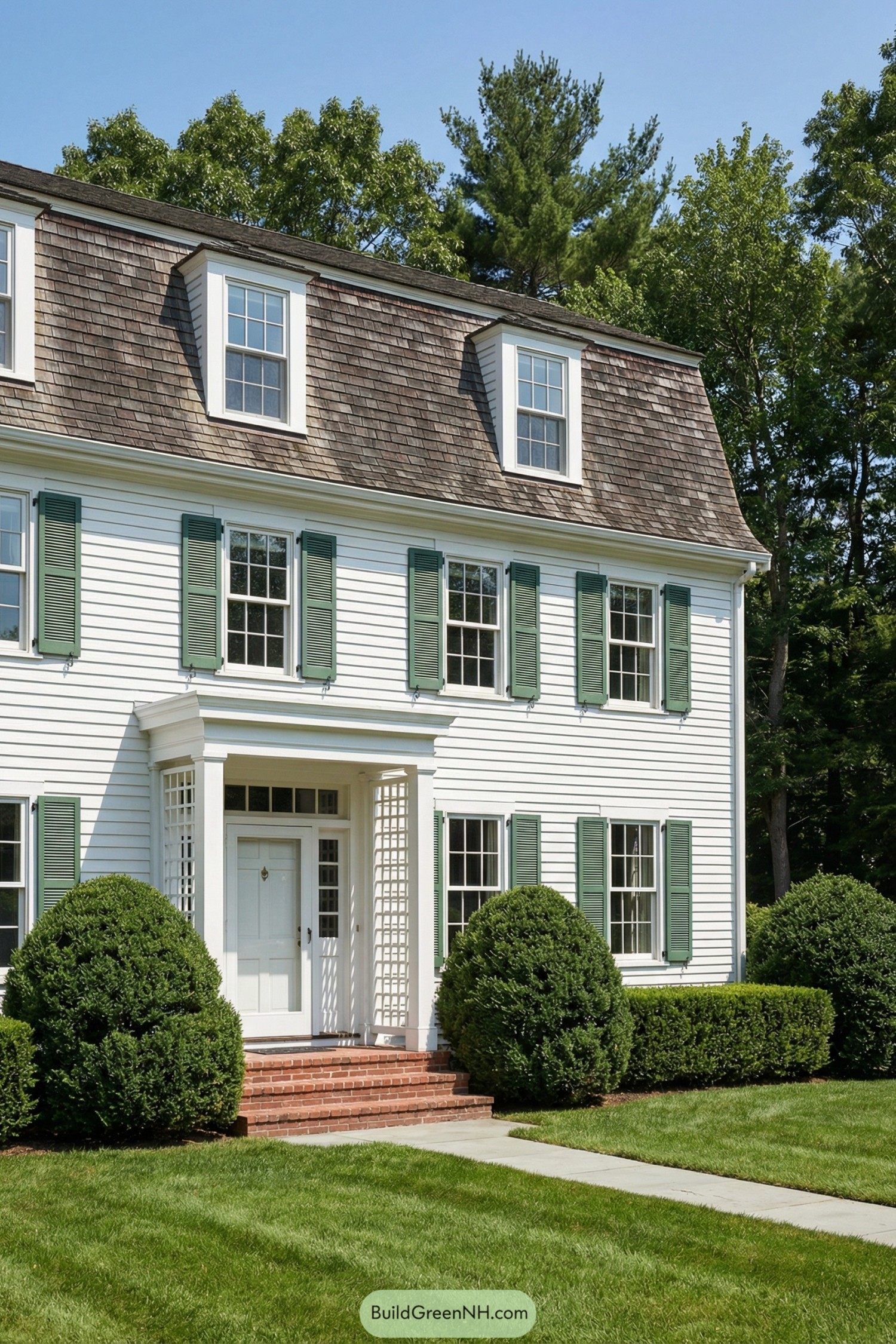 White colonial house with cedar mansard roof and green shutters