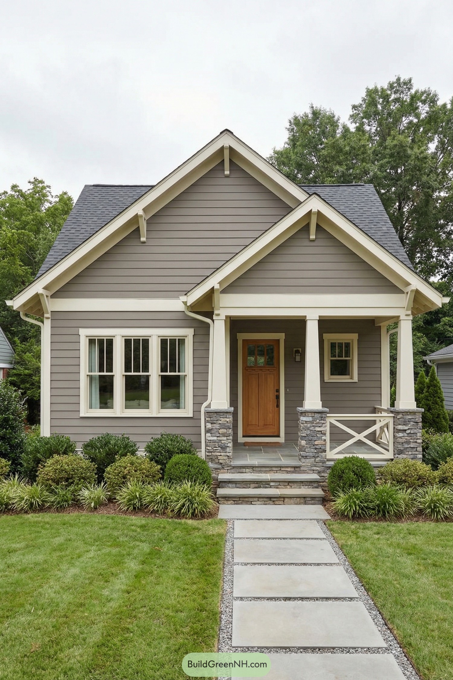 Compact gray craftsman cottage with gabled roof, stone porch columns, and tidy front landscaping along a concrete path