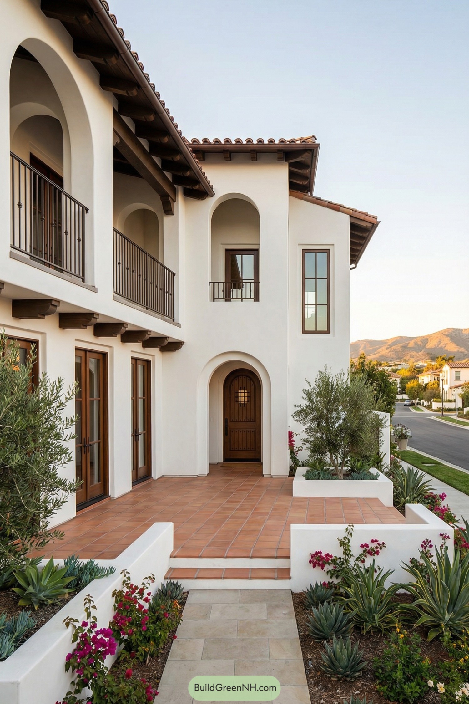 Two story white stucco Spanish style home with terracotta entry terrace arched openings and dark wood accents facing a suburban street