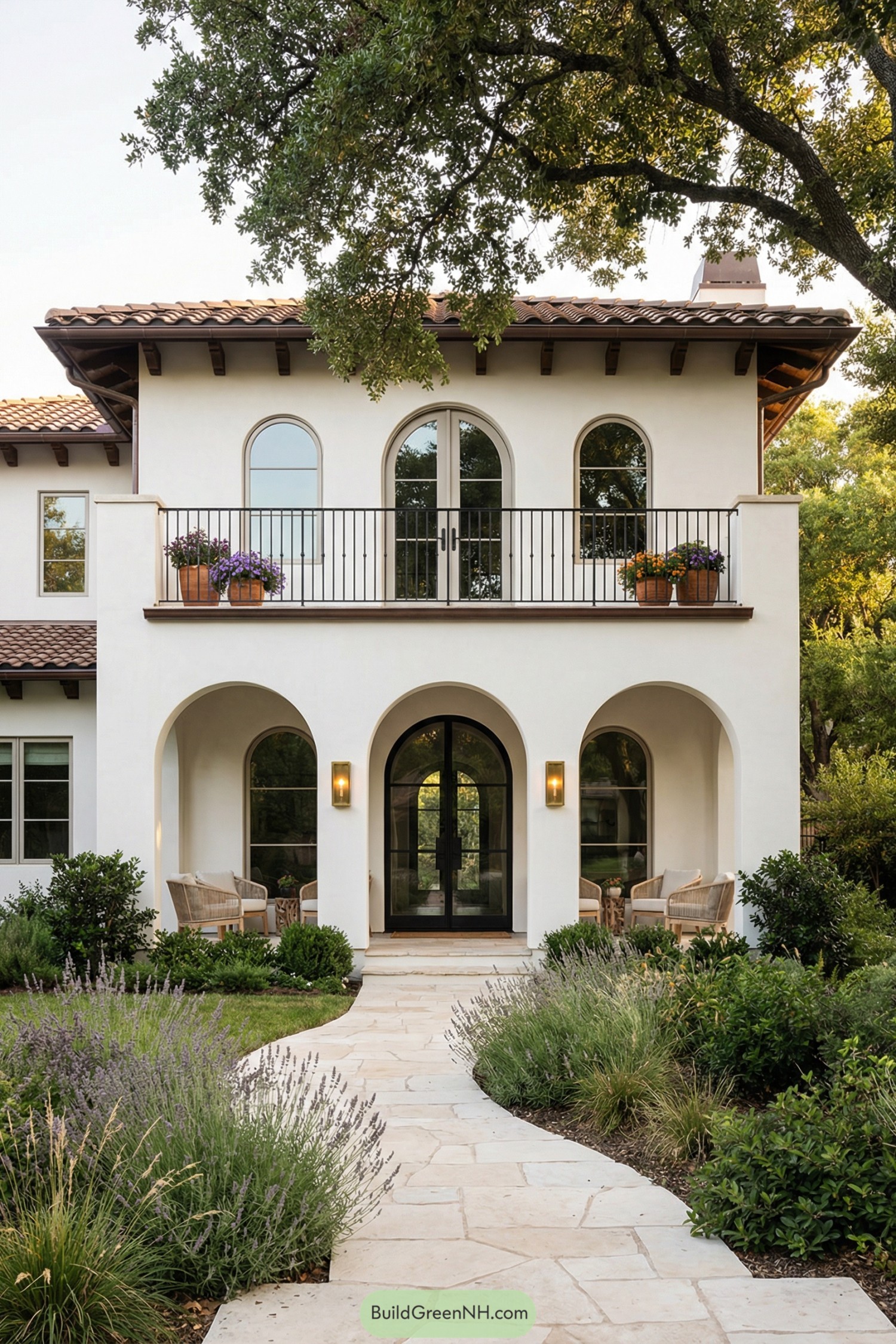 Two story white stucco Spanish style house with arched entry, balcony, and lush front garden path
