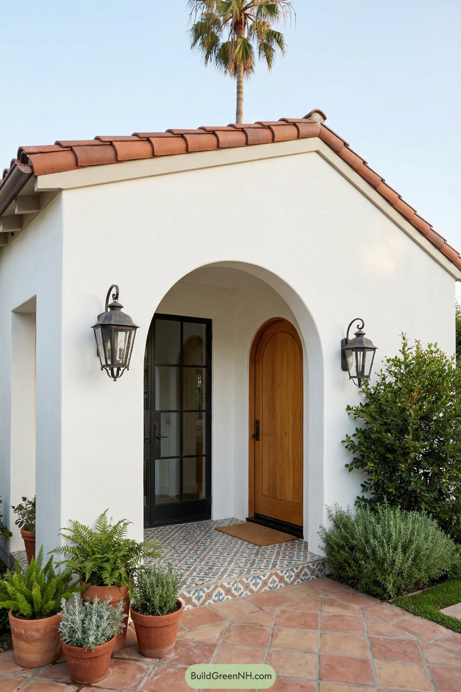 Compact Spanish style porch with arched entry, wood door, patterned tile and potted plants