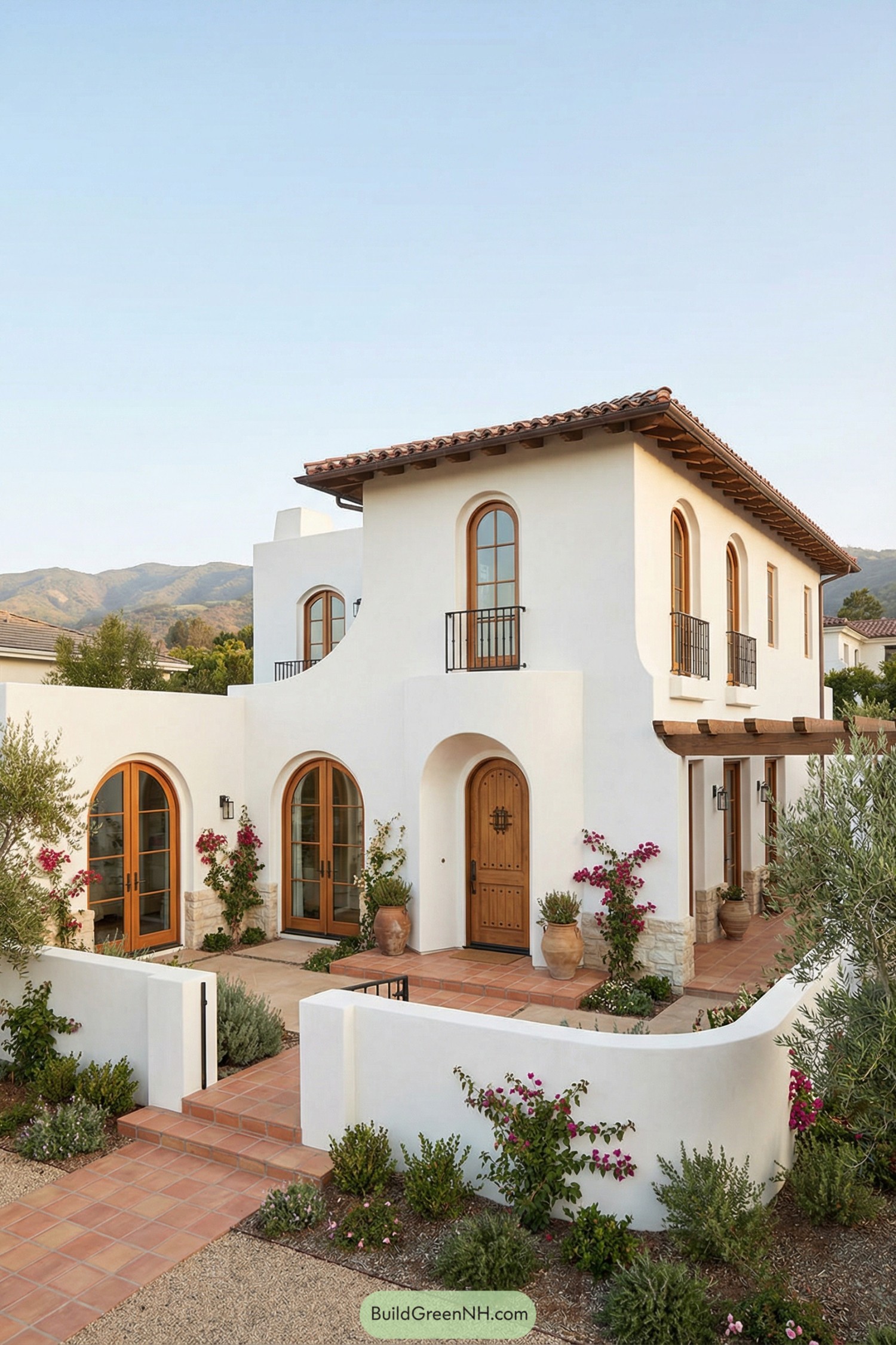 Two story white stucco Spanish style house with arched wood doors, balconies, and terracotta patio