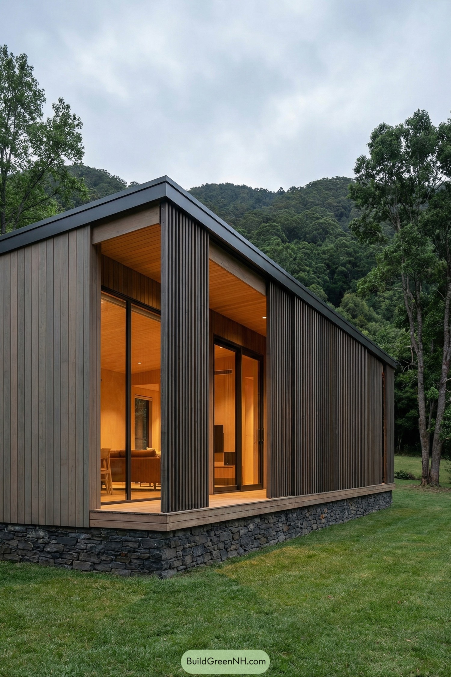 Modern timber cabin with tall glass doors and vertical wood cladding set on a stone base in a forest clearing