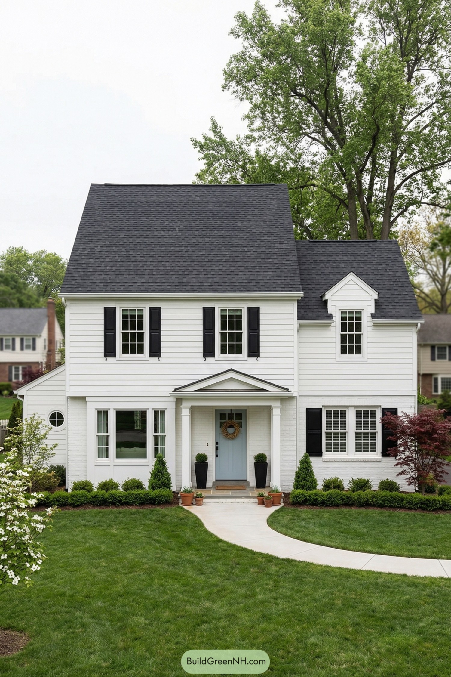 White colonial style house with black shutters soft blue front door and curved sidewalk through a manicured lawn