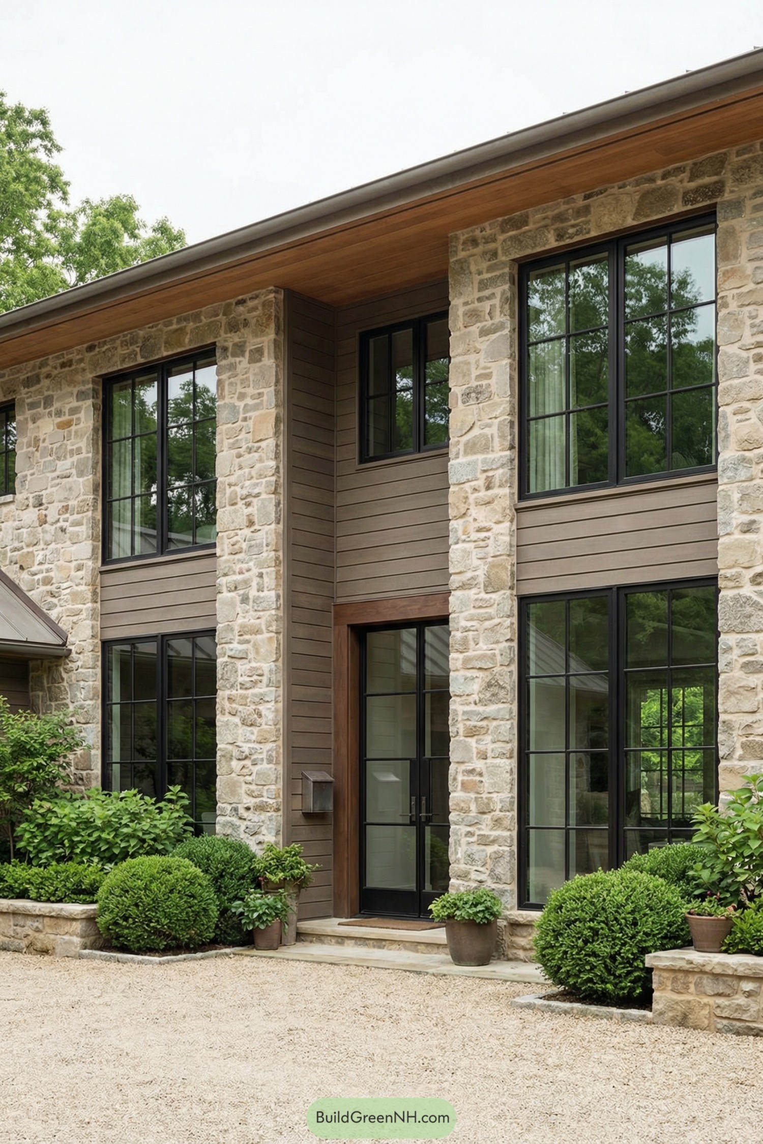 Stone and wood modern house front with tall black grid windows and lush shrubs