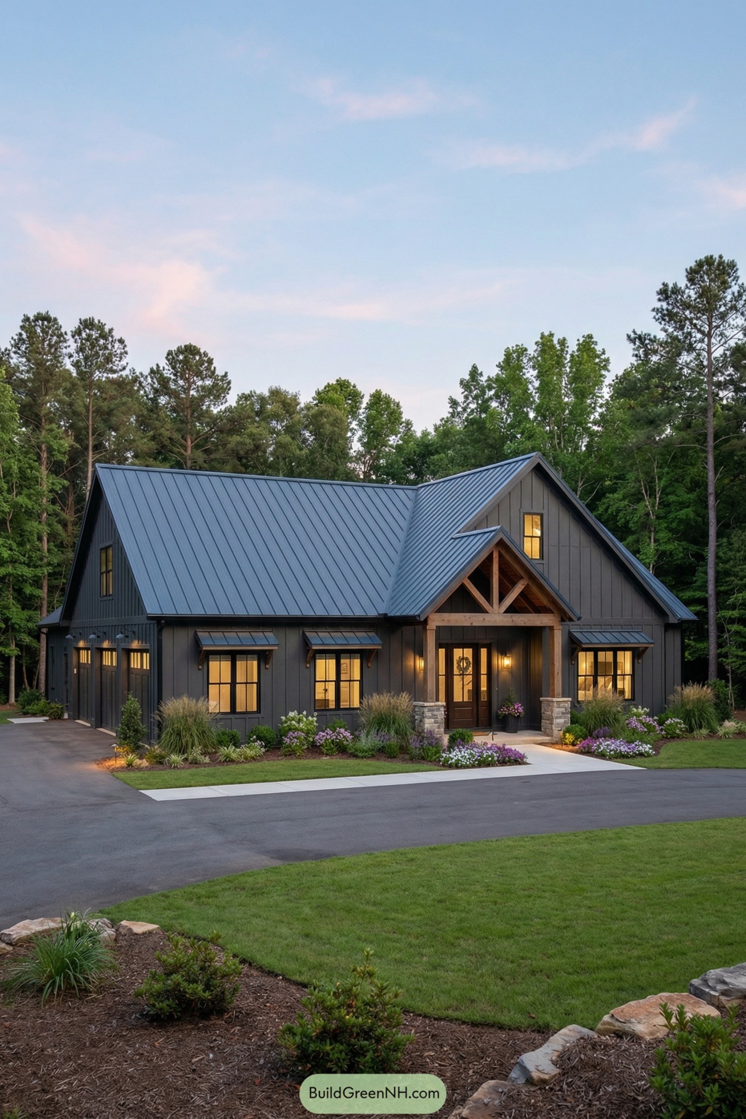 Dark gray single story barndominium with metal roof, timber entry porch, and landscaped front yard in wooded setting