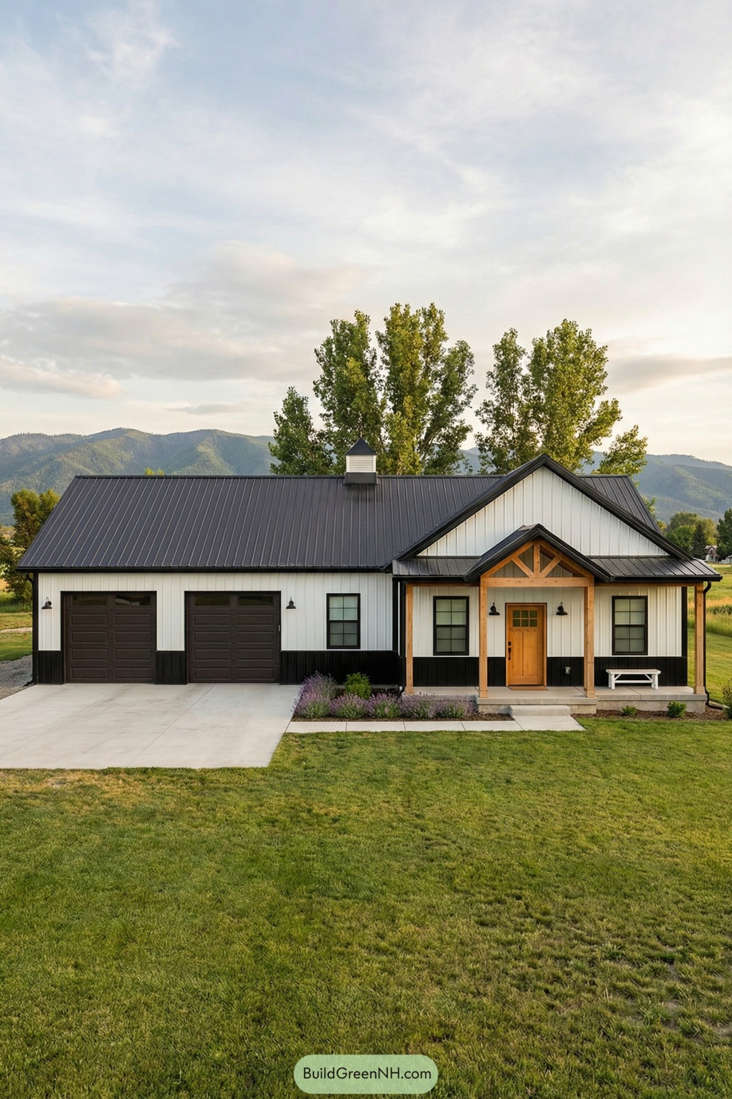 Single story barndominium with black metal roof and front porch in a wide green field