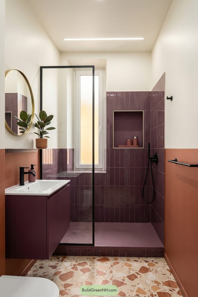 high-res photo of small bathroom interior with compact plan, bold contemporary color-block style, palette of creamy white, terracotta, and deep plum accents, crisp boxed niche geometry and a minimal partition, walls split between terracotta paint and plum-toned tile in the shower, narrow vertical window with frosted glass and warm daylight, terrazzo floor with terracotta chips, ceiling with a slim linear light, materials in terrazzo, glazed tile, and powder-coated metal, a compact vanity in plum lacquer with integrated sink, circular mirror with thin brass edge, accessories including a color-matched tray and modern canisters, a small rubber plant for contrast, and black hardware to anchor the palette, single photo, high-resolution, real estate staging photography, strictly no collages.