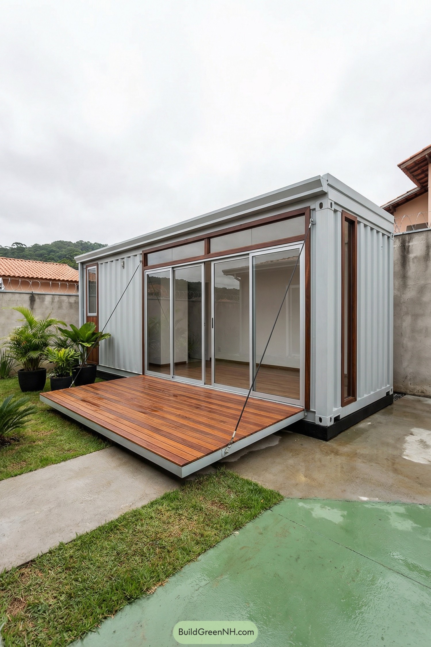Small white container house with sliding glass doors and a floating wood deck in a walled courtyard