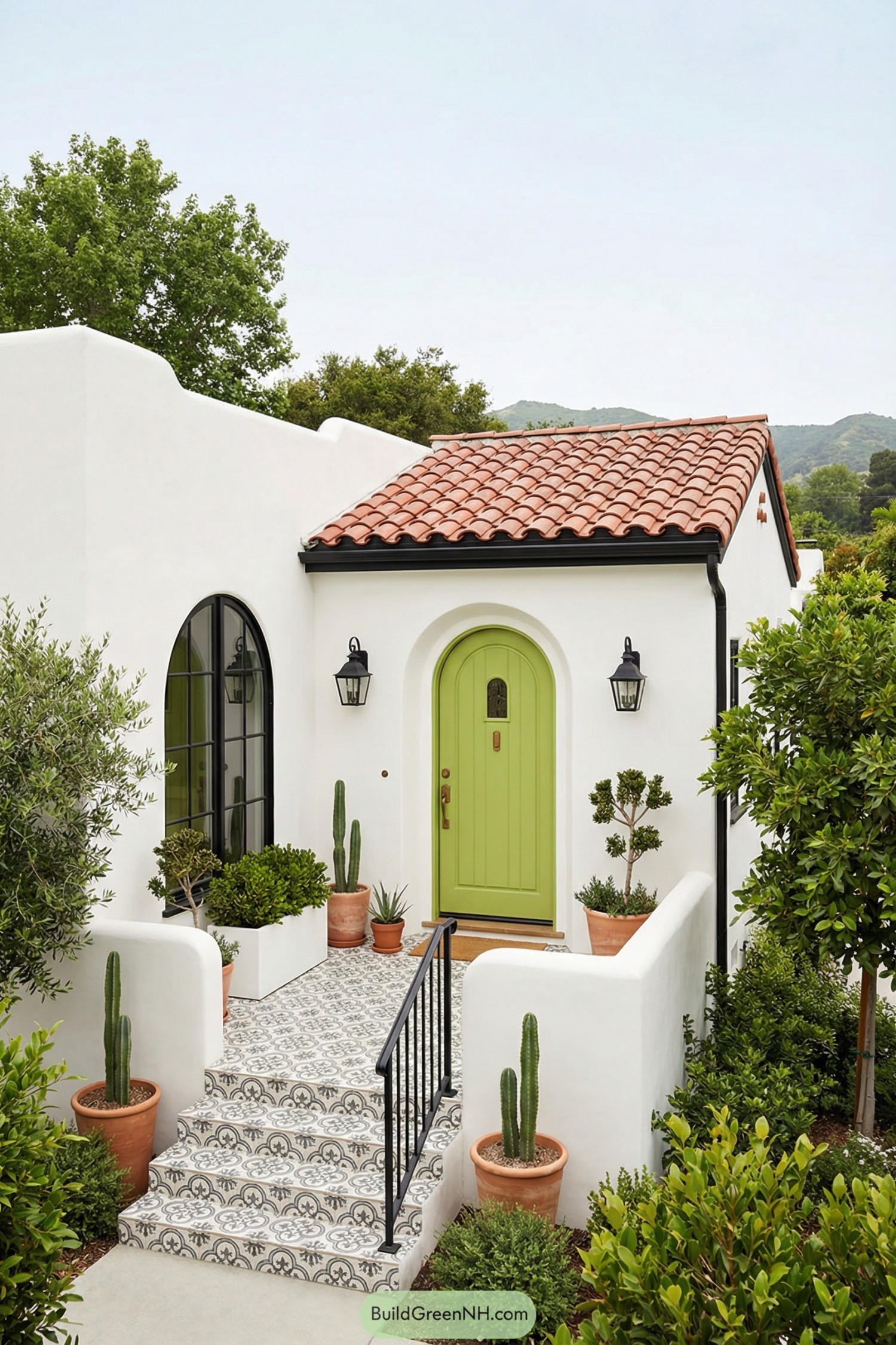White stucco Spanish cottage with red tile roof, lime green arched door, patterned tile steps, and terracotta pots of greenery