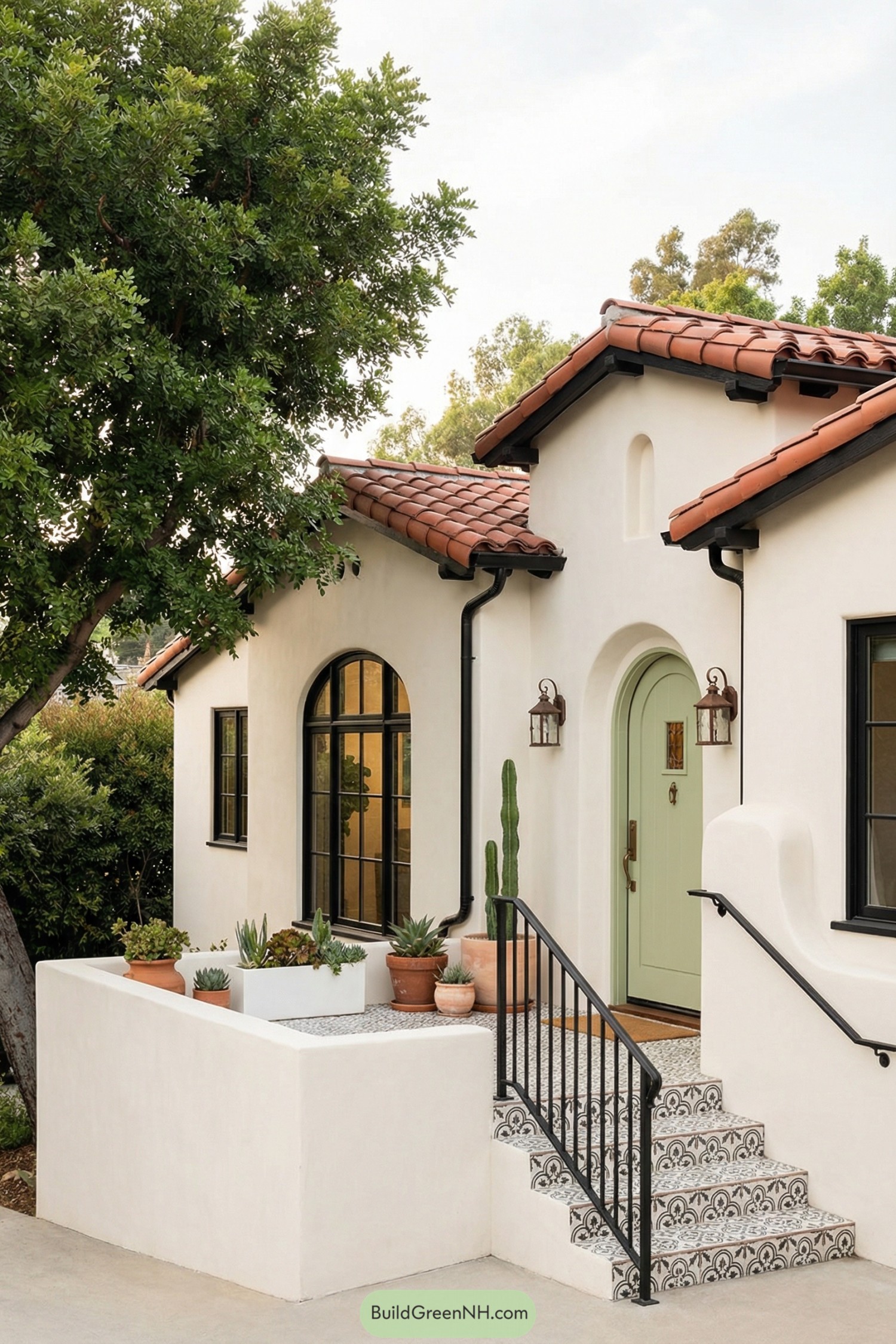 Creamy stucco cottage with red tile roof and sage green arched door framed by patterned tile steps and potted succulents